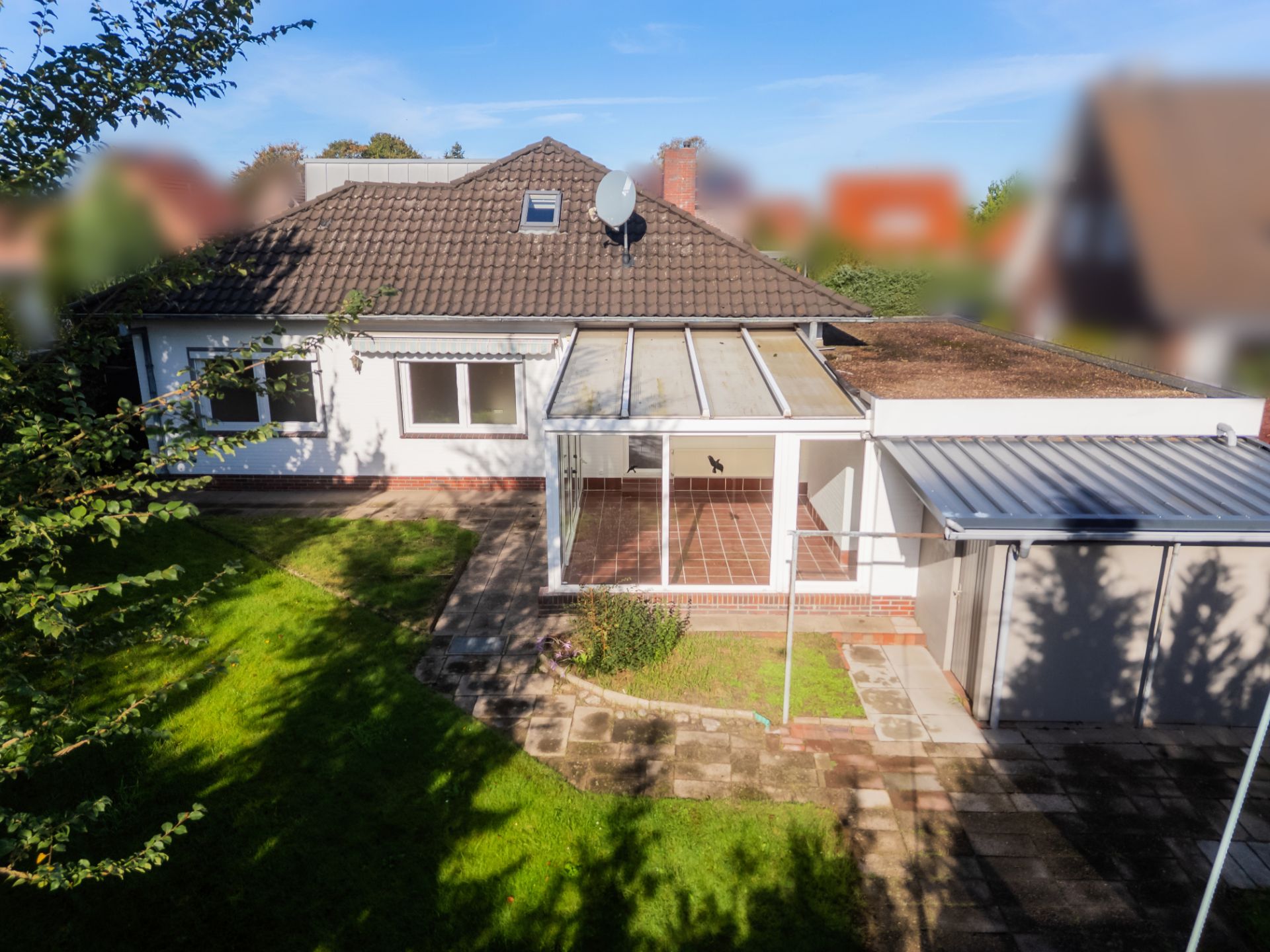 Einfamilienhaus mit Wintergarten, Terrasse, Garage und gepflegtem Garten bei Tageslicht.