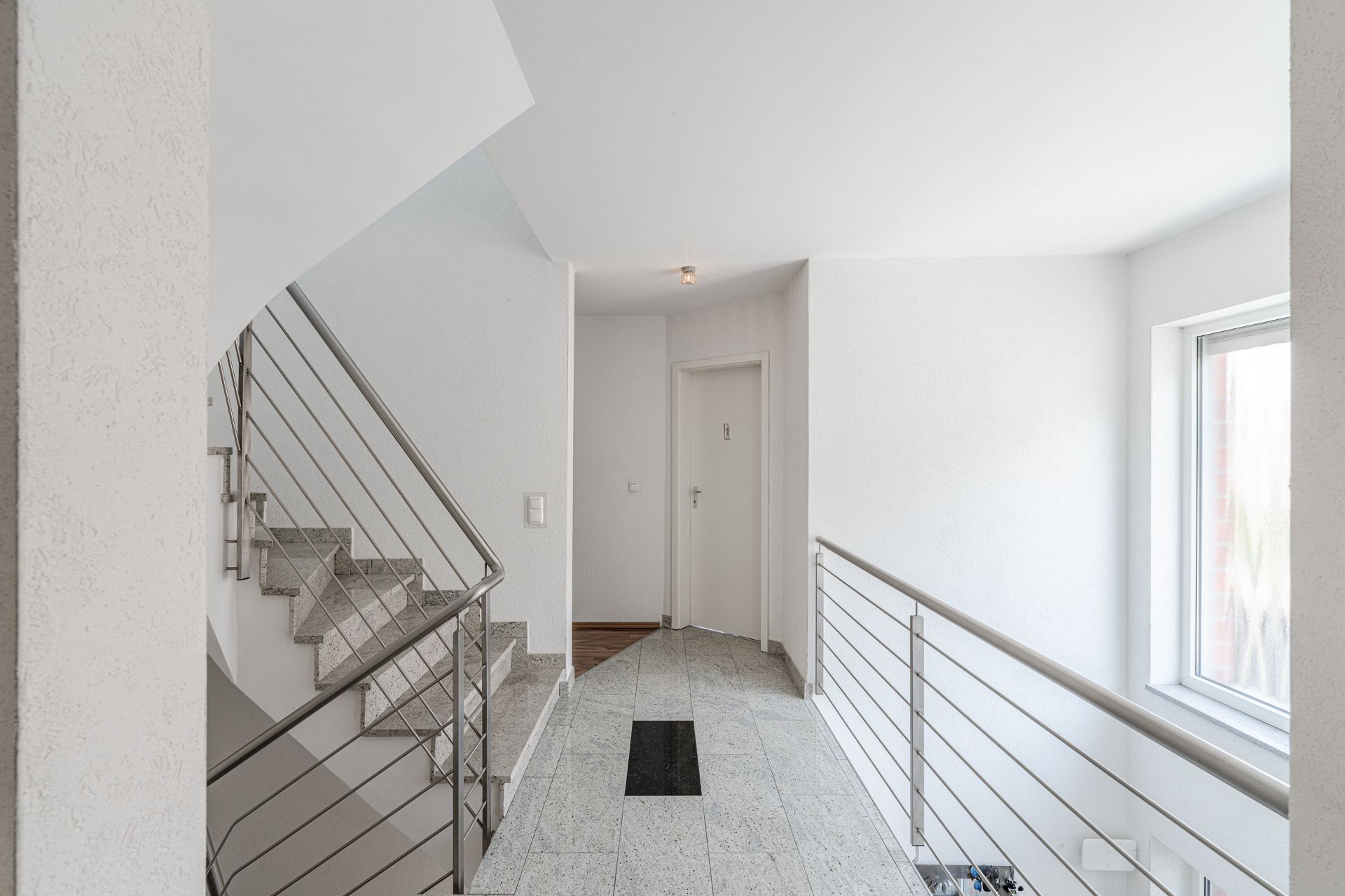 Heller Flur mit Treppe, Geländer und Fenster in einem Wohngebäude.