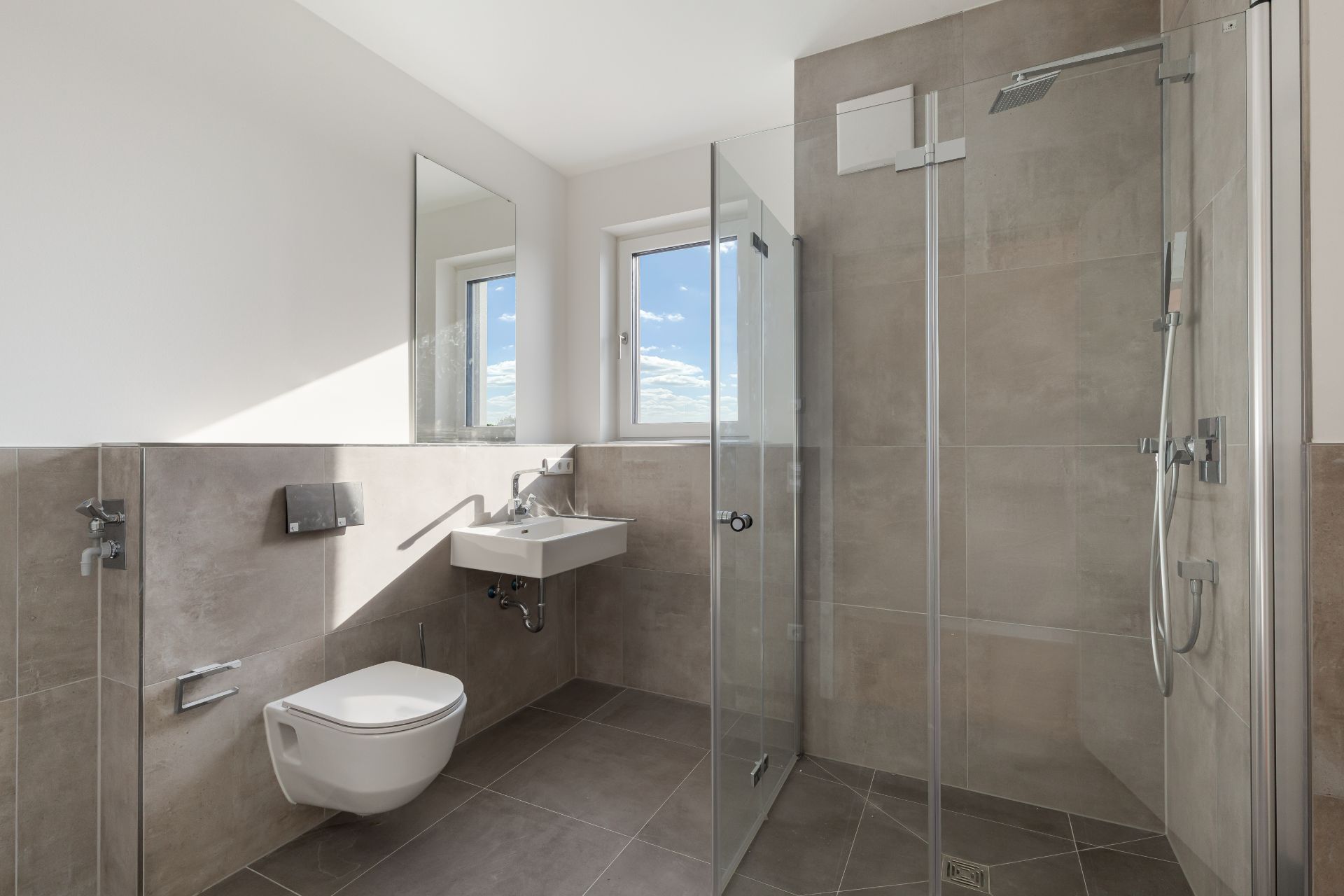 Modernes Badezimmer mit Dusche, Wandtoilette, Waschbecken, Spiegel und Fenster.