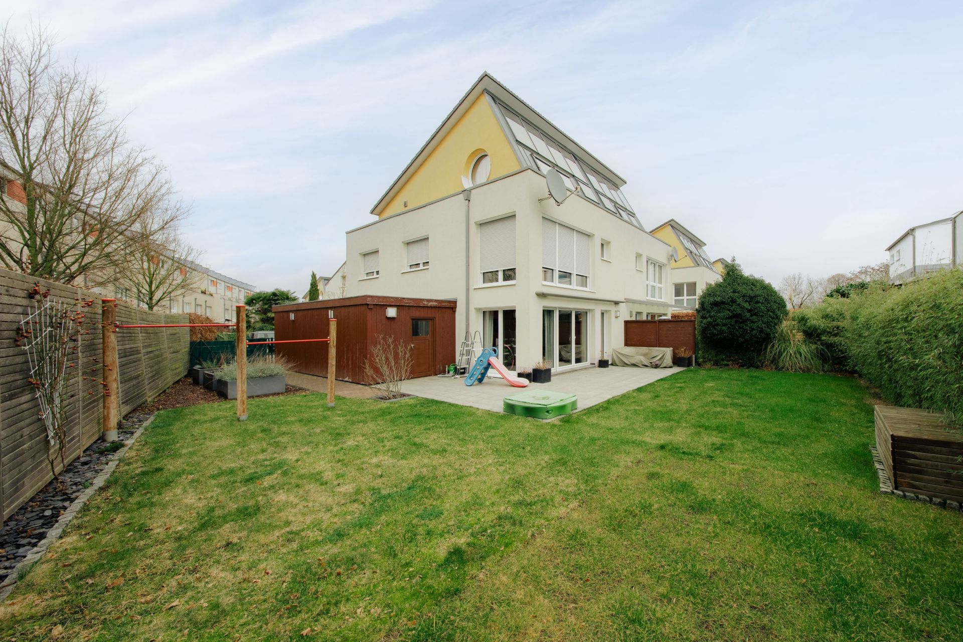 Modernes Wohnhaus mit großem Garten, Terrasse, Rutsche und Sandkasten.