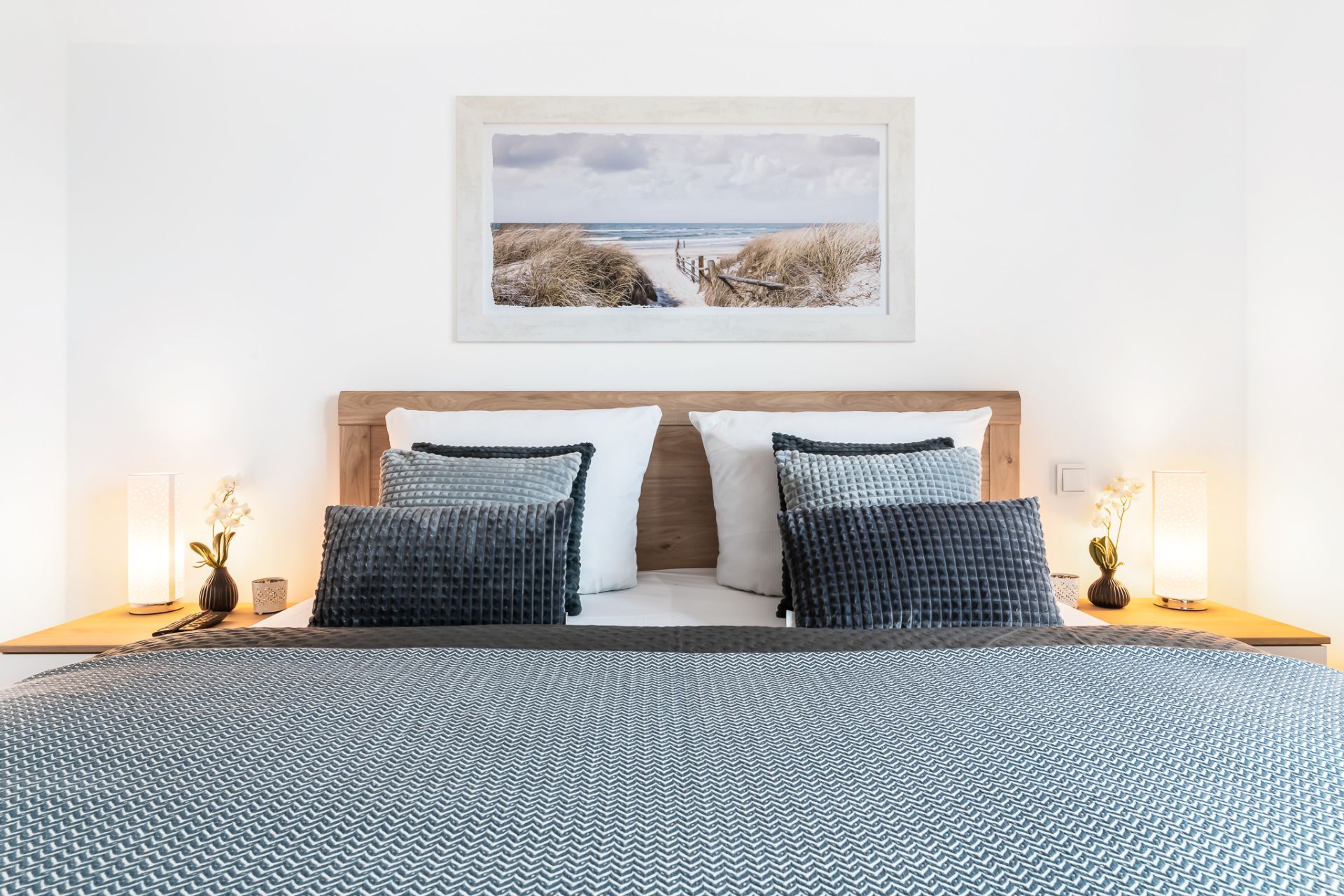 Modernes Schlafzimmer mit Doppelbett, grauer Bettwäsche, zwei Nachttischen und Bild an der Wand.