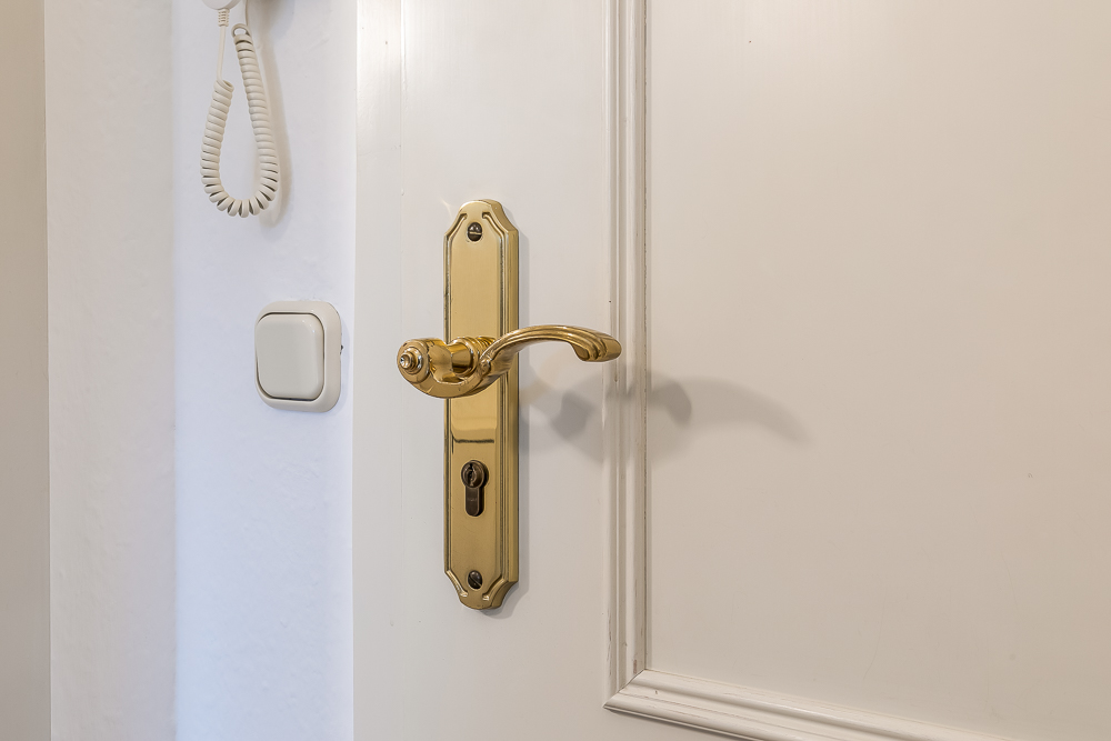 Nahaufnahme eines weißen Türblatts mit goldenem Griff und Lichtschalter an der Wand.