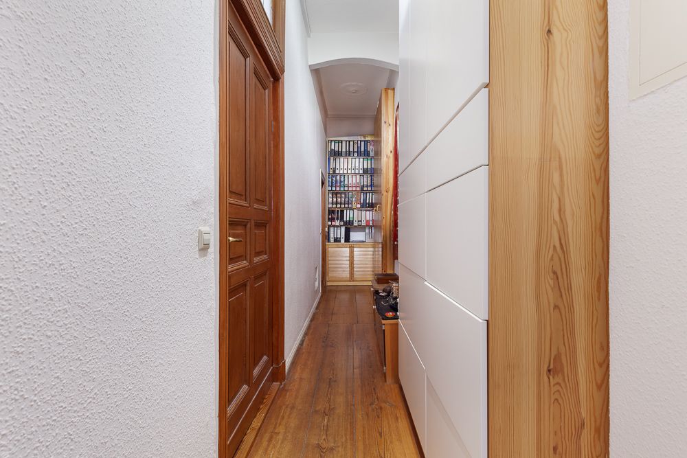 Schmaler Flur mit Holzboden, links Holztür, rechts weißer Schrank, am Ende Bücherregal.
