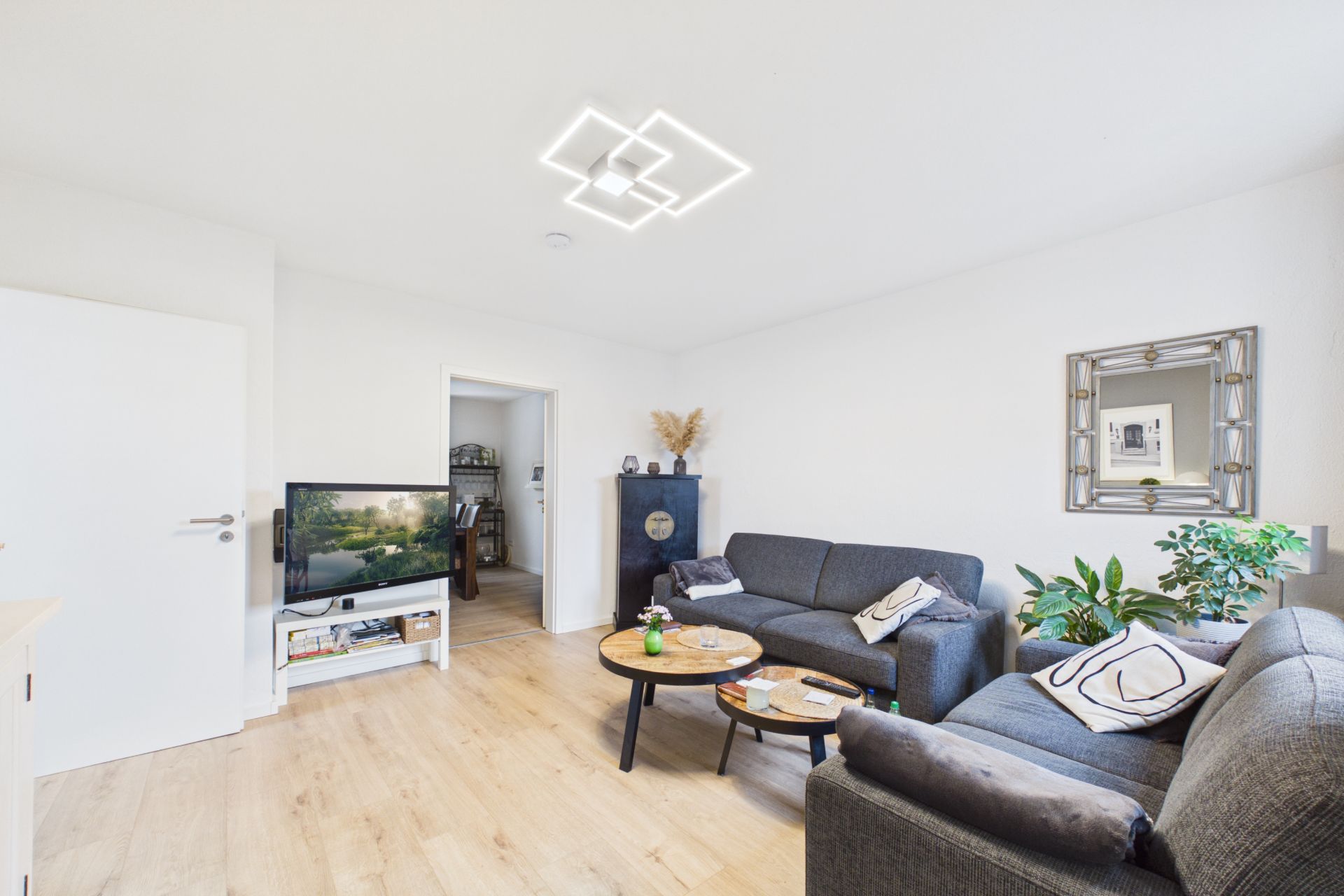 Helles Wohnzimmer mit zwei Sofas, Couchtisch, Fernseher und Zimmerpflanzen.