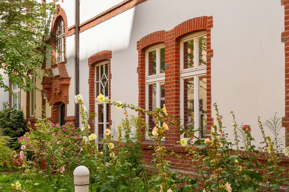 Fassade eines Wohnhauses mit roten Backsteinfenstern und buntem Vorgarten.