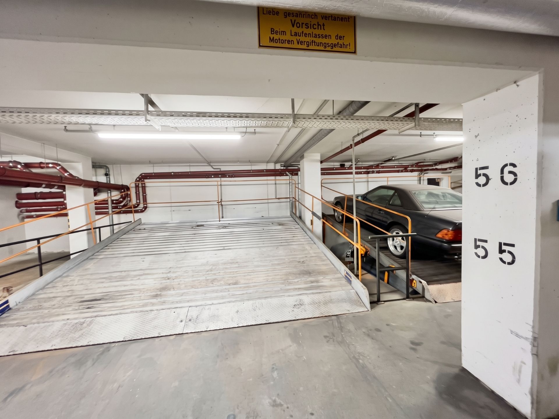 Parkplätze in einer Tiefgarage, einer ist mit einem schwarzen Auto belegt, Nummern 55 und 56 an der Säule.
