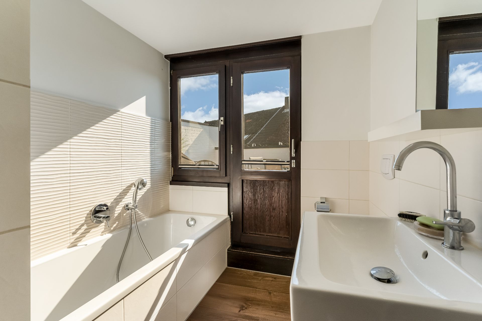 Modernes Badezimmer mit Badewanne, Waschbecken und großem Fenster mit Blick nach draußen.