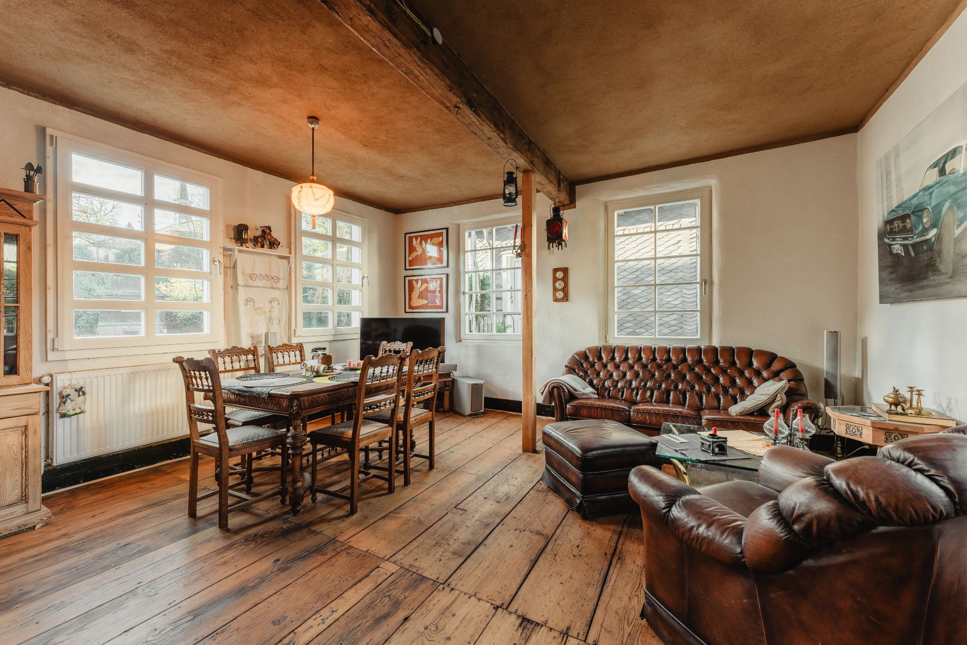 Gemütliches Wohnzimmer mit Ledersofas, Esstisch und Holzboden, große Fenster lassen viel Licht herein.