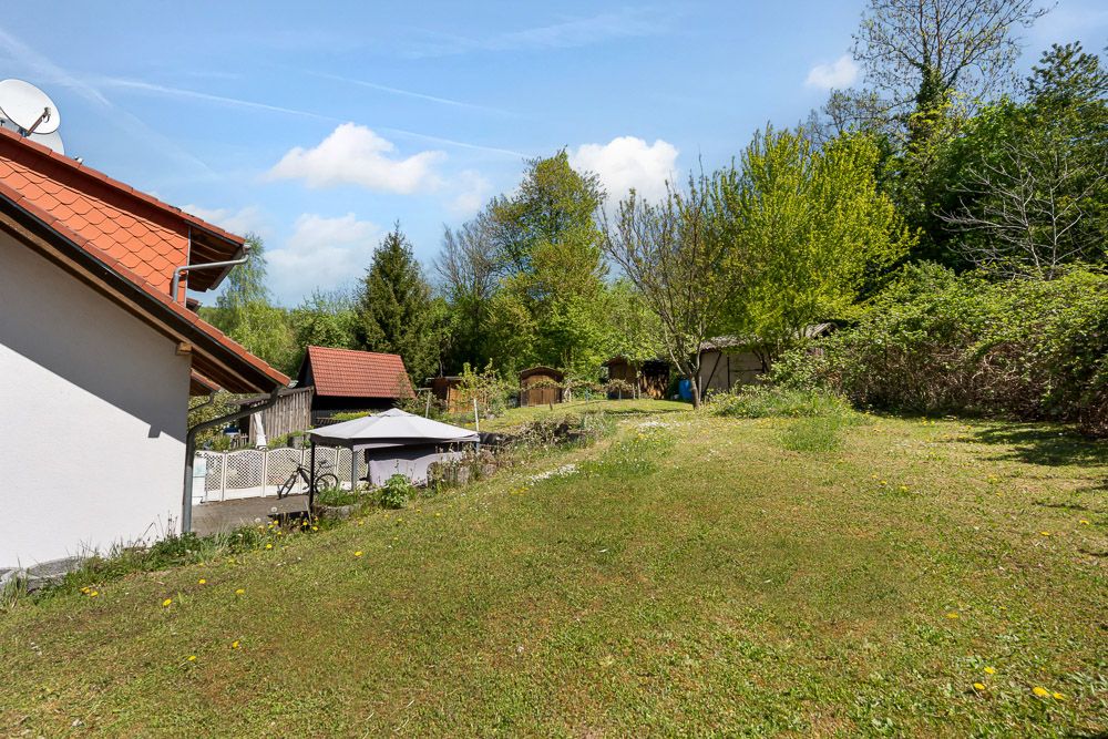 Garten mit Rasenfläche, Bäumen und einem Hausdach am linken Bildrand.