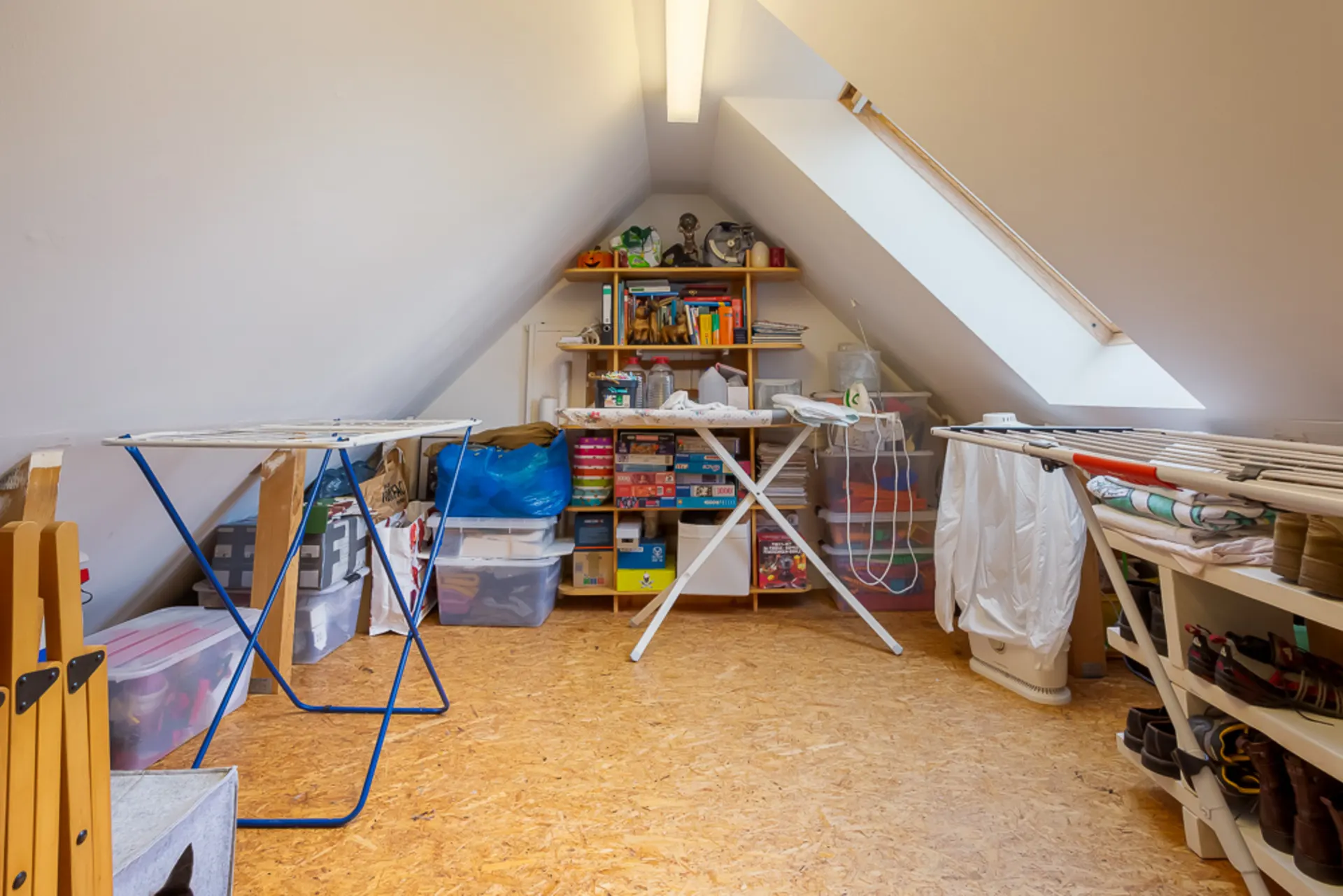 Dachzimmer mit Regalen, Wäschegestellen und Aufbewahrungsboxen unter einer Schräge.