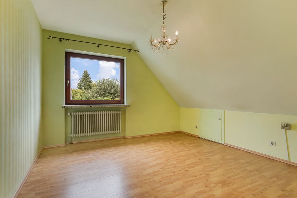 Leeres Zimmer mit Holzfußboden, gelben Wänden, großem Fenster und Kronleuchter.