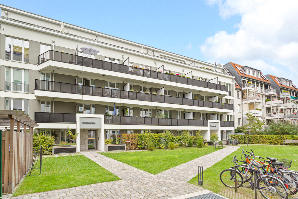Modernes Wohngebäude mit Balkonen, Grünfläche und mehreren Fahrrädern im Vordergrund.