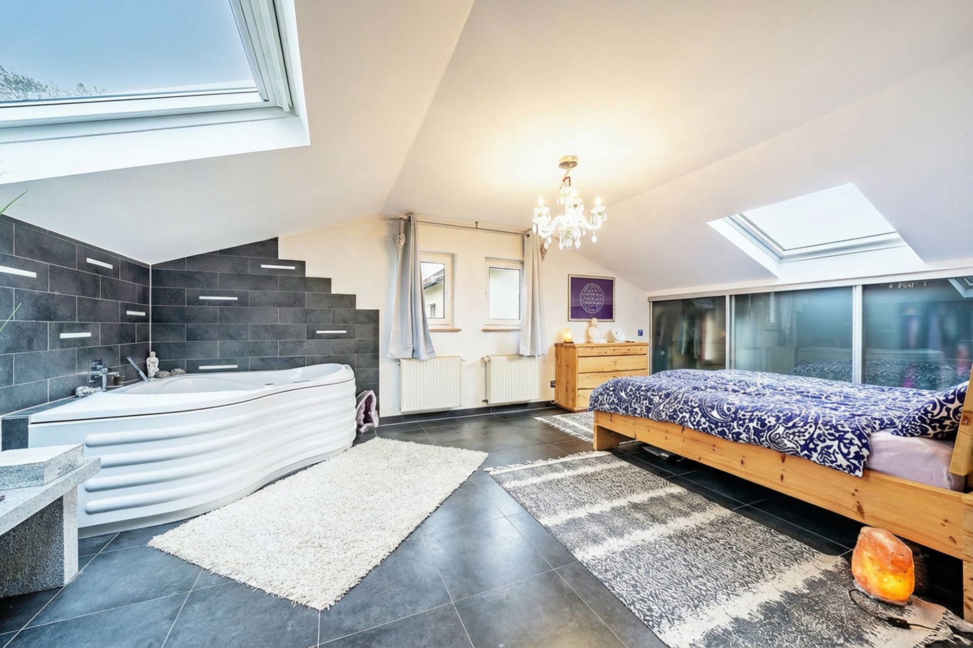 Modernes Schlafzimmer mit Badewanne, Dachfenster und Holzbett auf dunklem Fliesenboden.