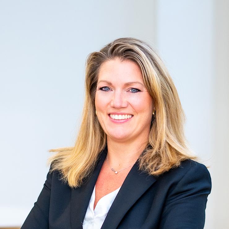 Frau mit blondem Haar und schwarzem Blazer steht mit verschränkten Armen und lächelt.