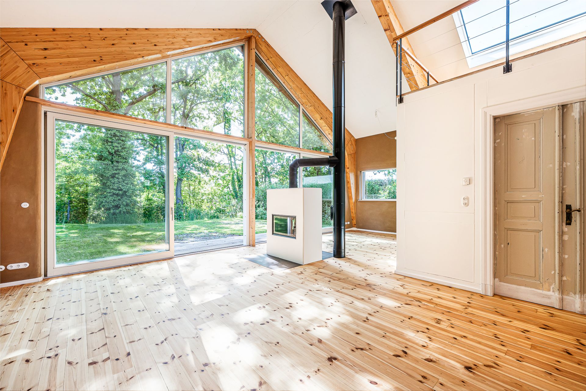 Helles Wohnzimmer mit großen Fenstern, Kaminofen und Holzfußboden, Blick auf Garten.