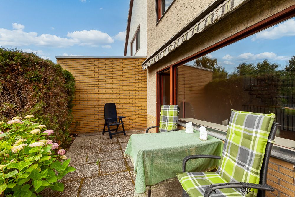 Möblierte Terrasse mit grün karierten Stühlen, Tisch und Markise an einem Wohnhaus.