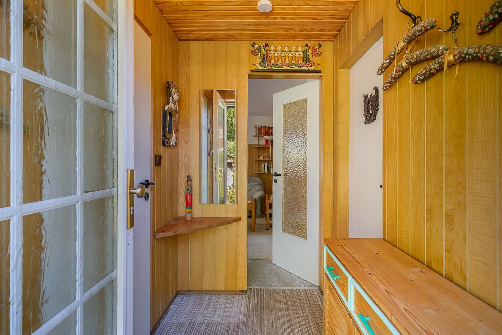 Holzverkleideter Flur mit Spiegel, Garderobenhaken und offenen Türen zu weiteren Zimmern.