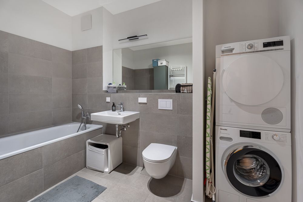 Modernes Badezimmer mit Badewanne, Waschbecken, Toilette und Waschmaschine mit Trockner.