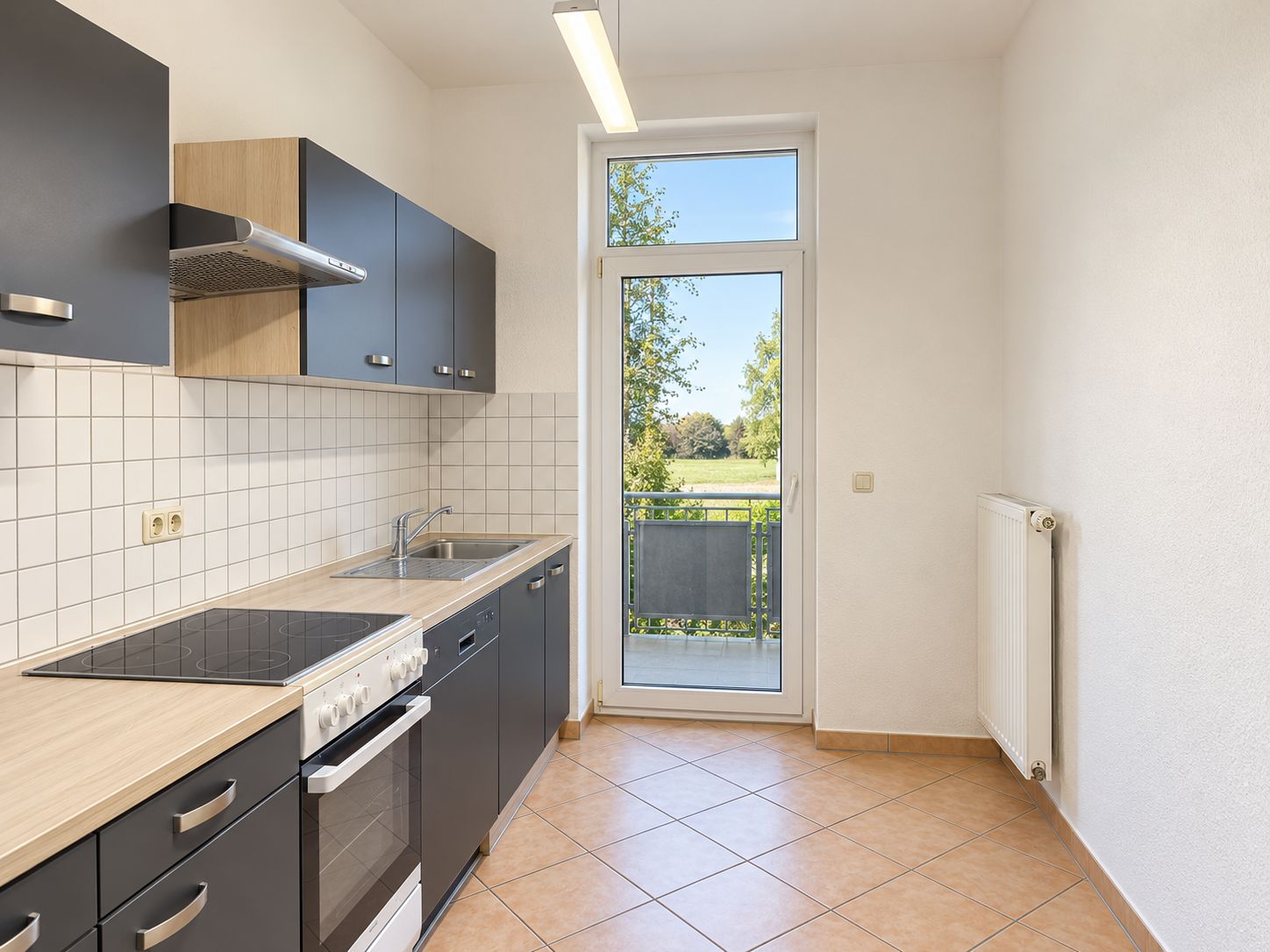 Helle Küche mit dunklen Schränken, Herd, Spüle und Zugang zu einem Balkon.