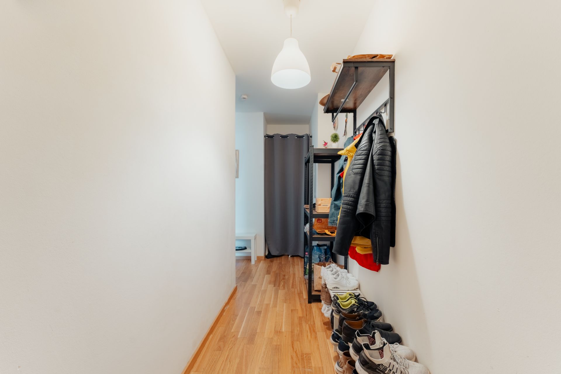 Schmaler Flur mit Holzboden, Garderobe, Schuhregal und aufgehängten Jacken.