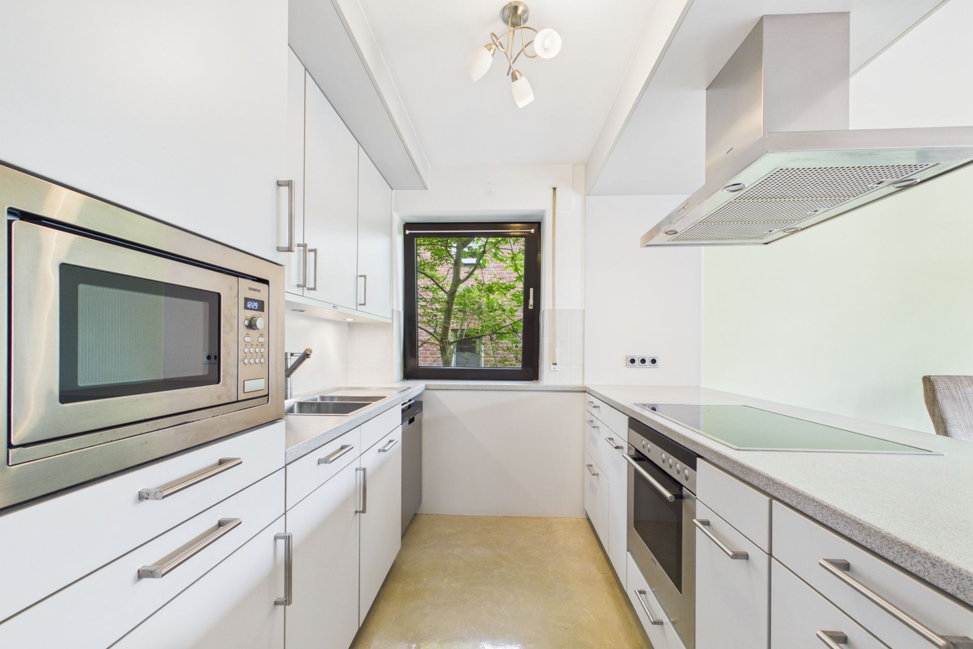 Moderne weiße Einbauküche mit Fenster, Backofen, Herd und Mikrowelle.