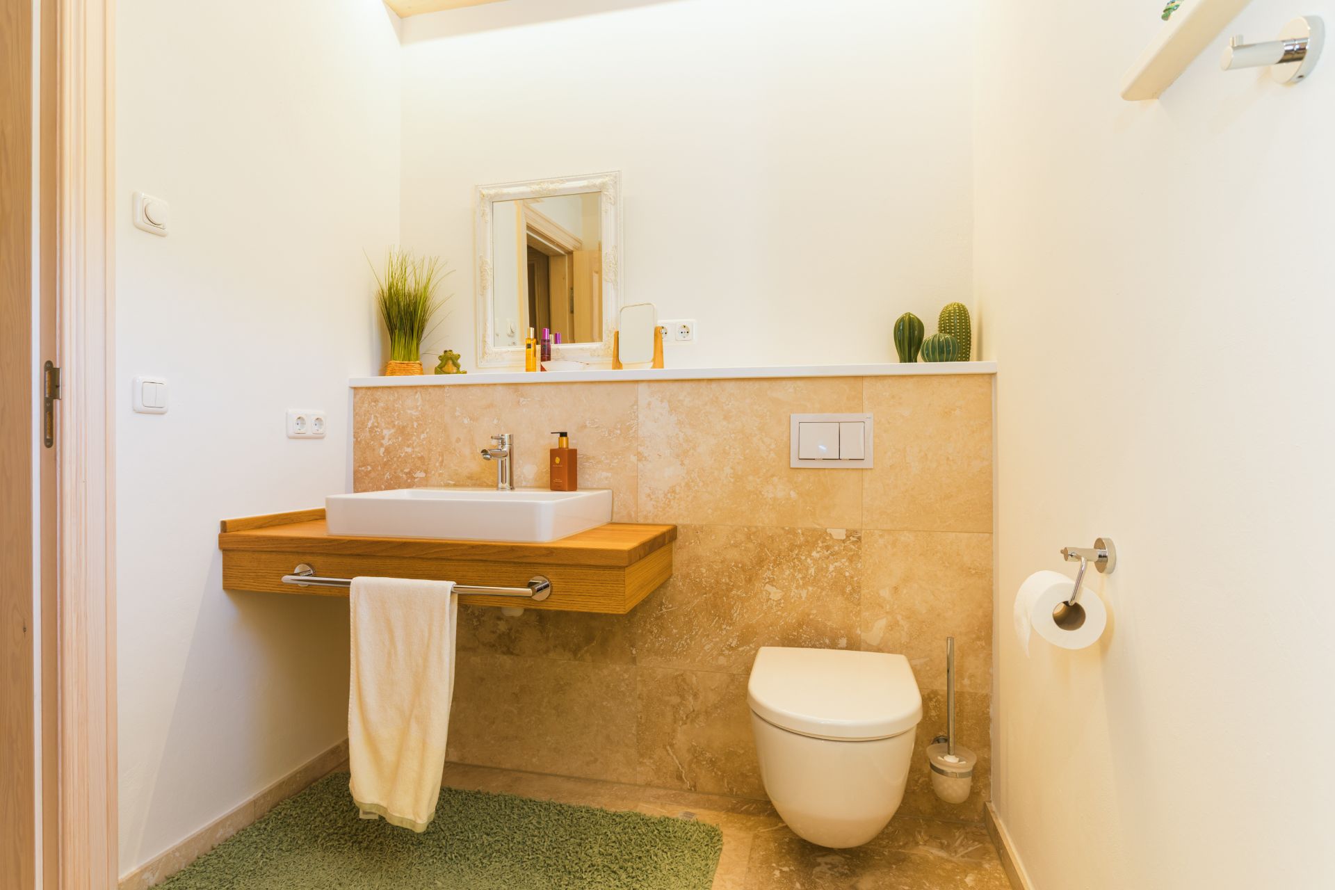 Modernes Badezimmer mit Waschbecken, Wandtoilette, Spiegel und grüner Matte.