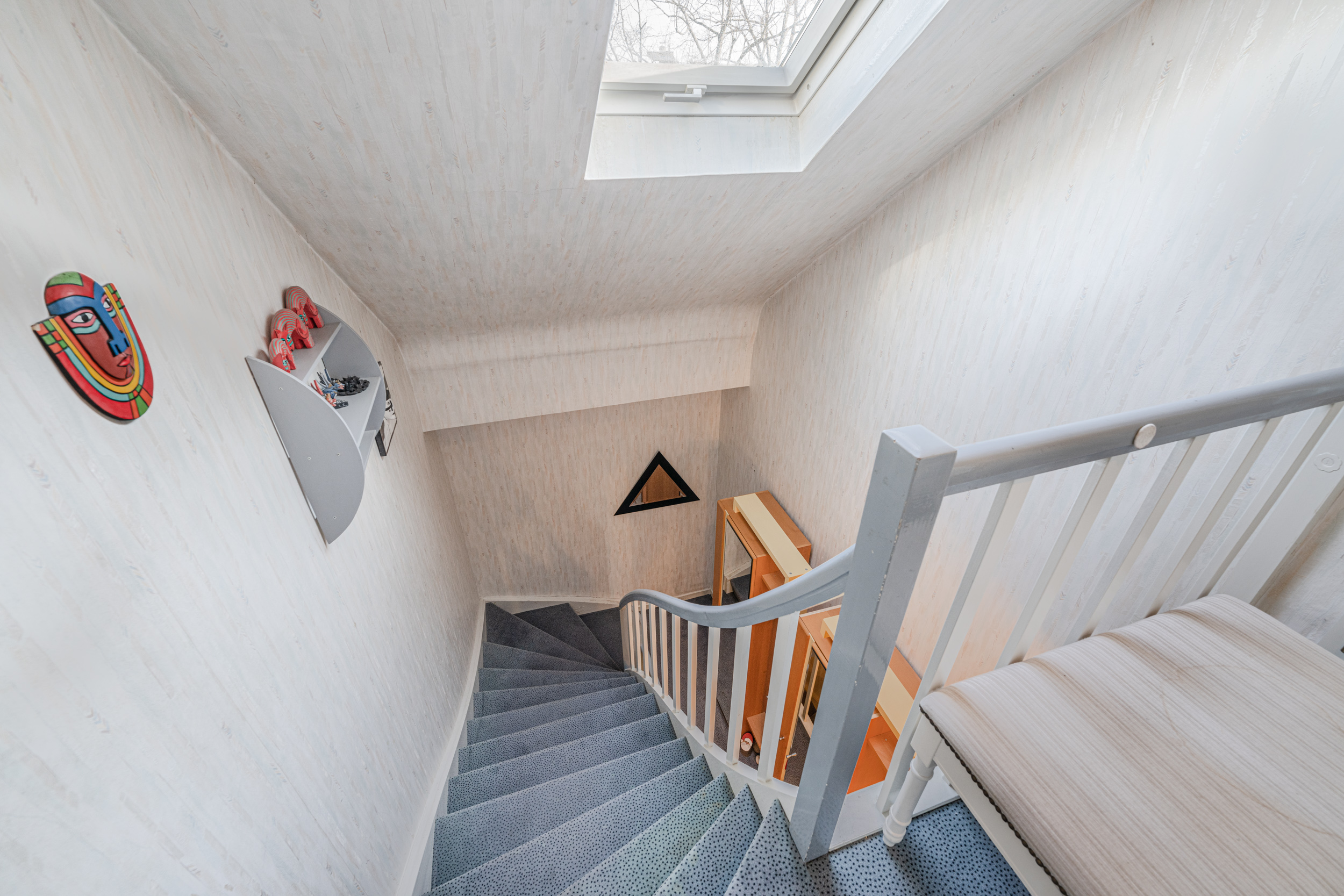 Helle gewendelte Treppe mit Teppich, Dachfenster und Wanddekorationen in einem Wohnhaus.