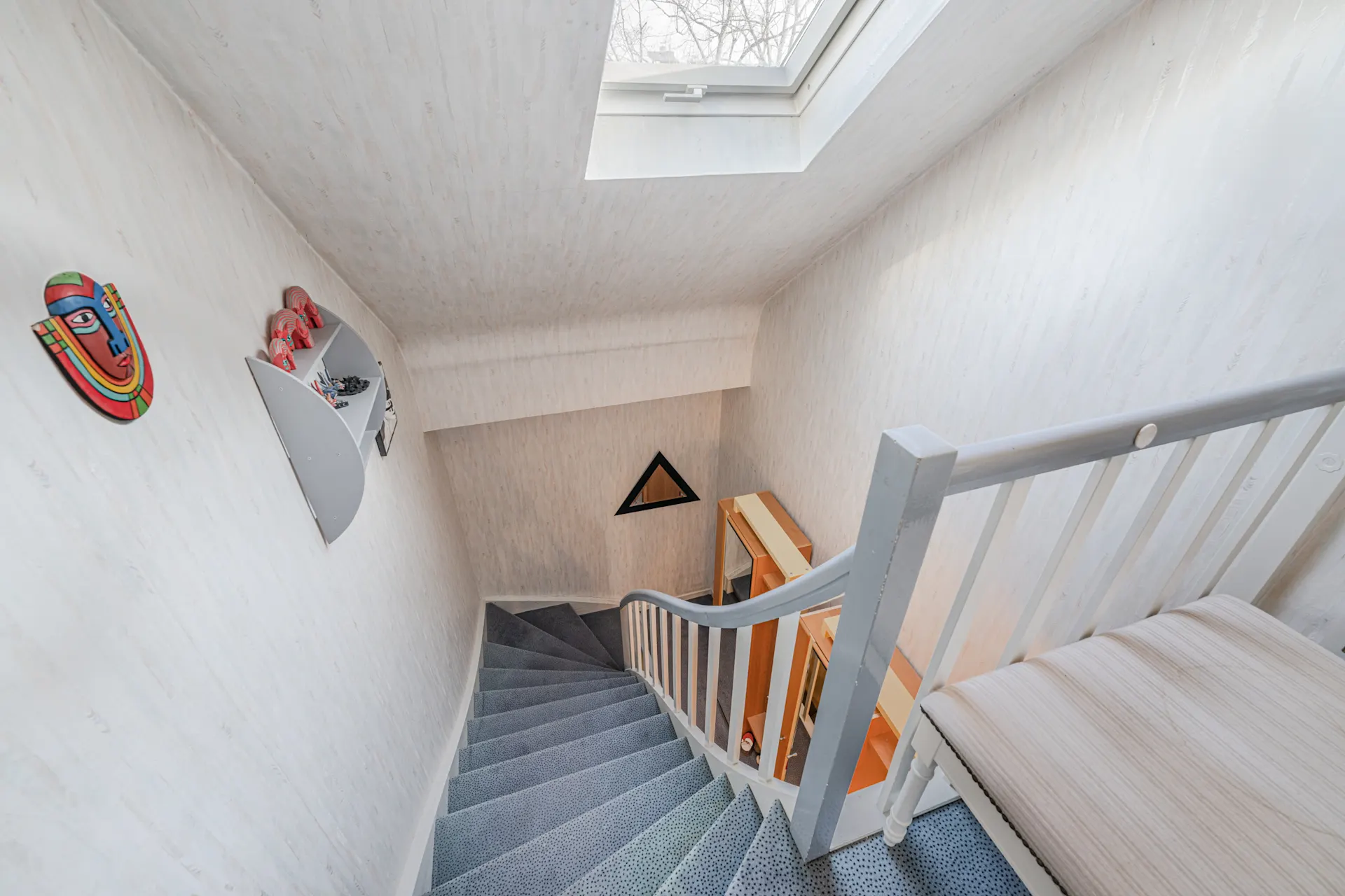 Helle gewendelte Treppe mit Teppich, Dachfenster und Wanddekorationen in einem Wohnhaus.