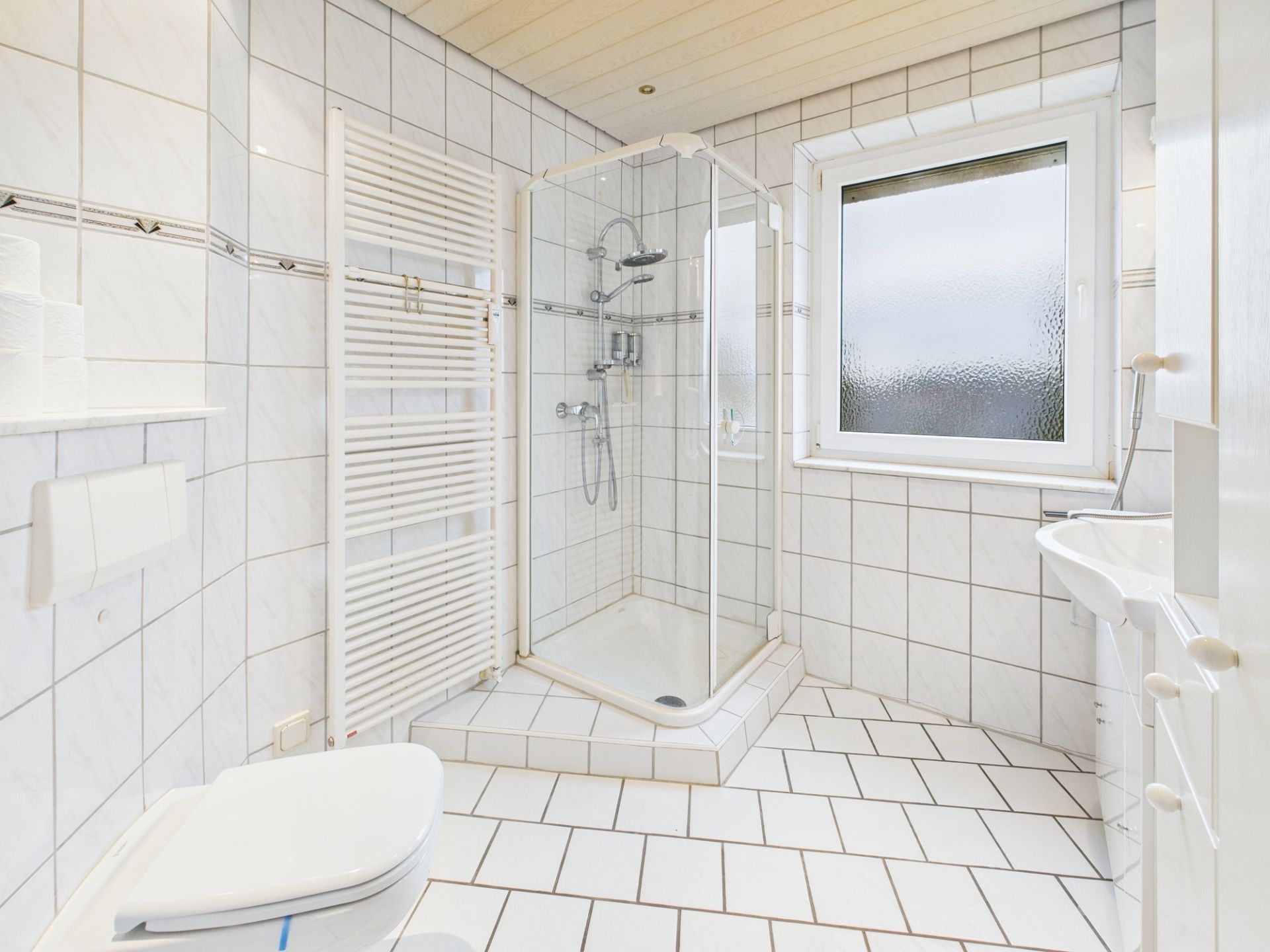 Helles Badezimmer mit Dusche, Waschbecken, WC, Fenster und Handtuchheizkörper.