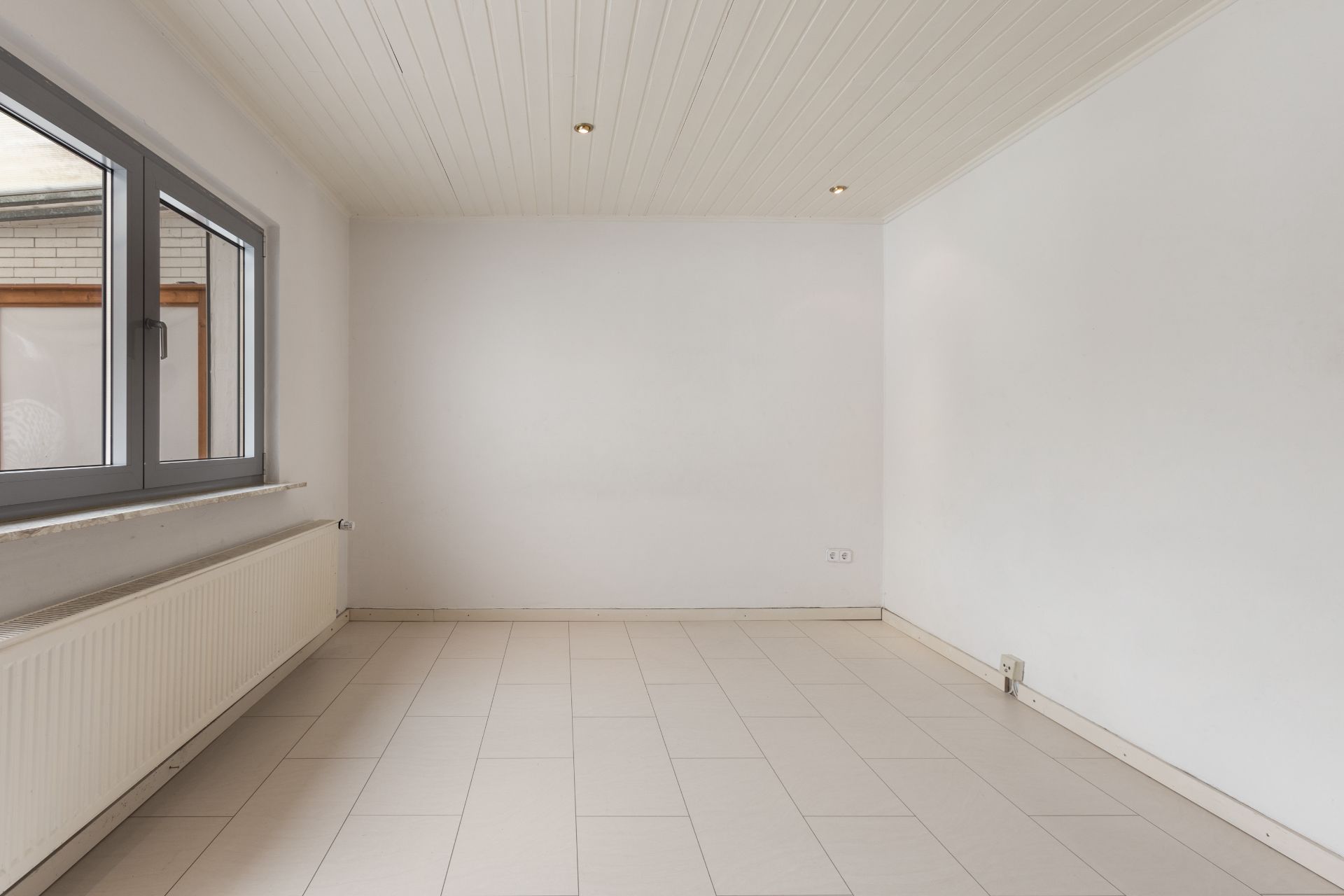 Leerer Raum mit weißen Wänden, Fliesenboden und großem Fenster.