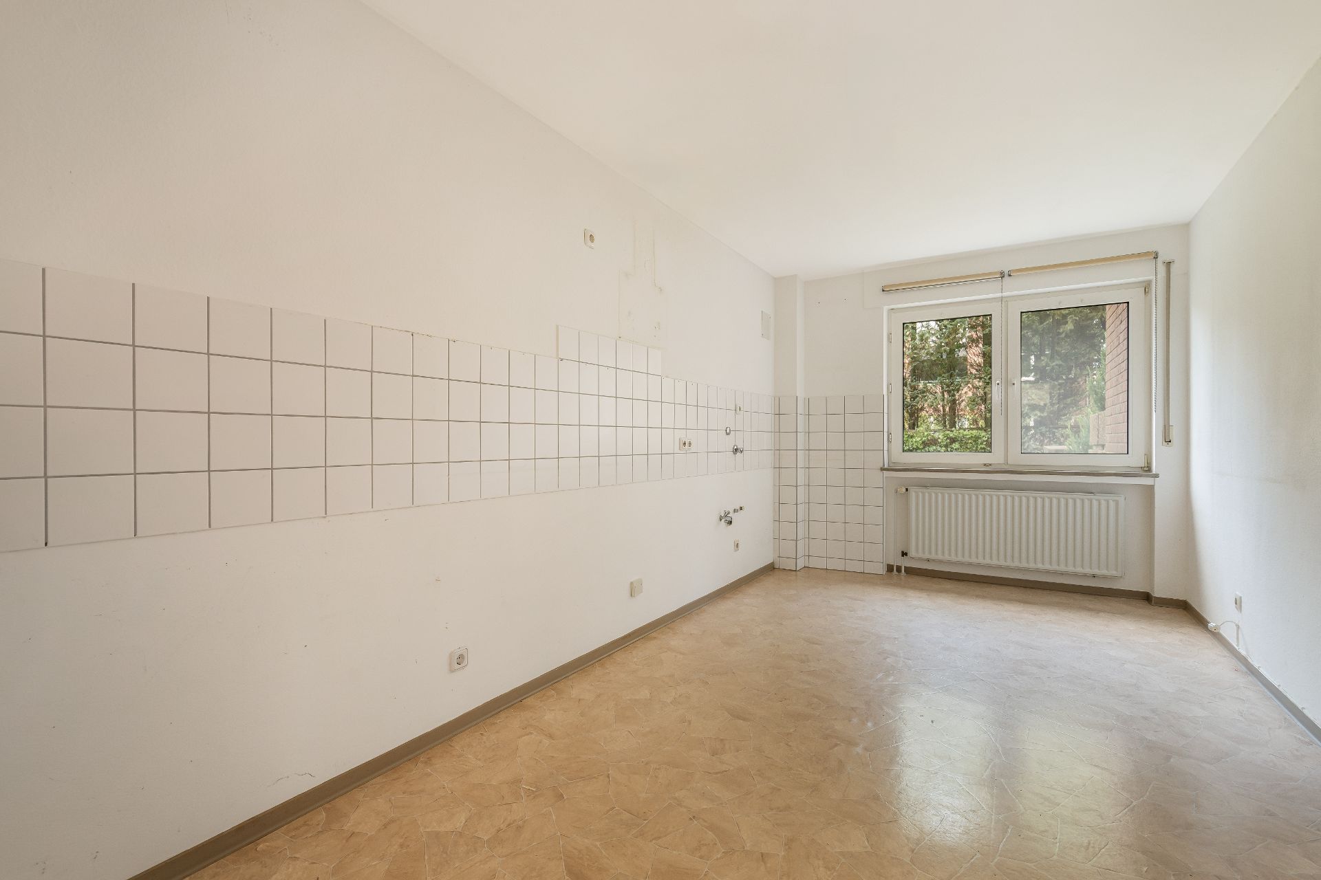 Leerer Raum mit Fliesenspiegel, großem Fenster und Heizkörper, ohne Möbel oder Geräte.