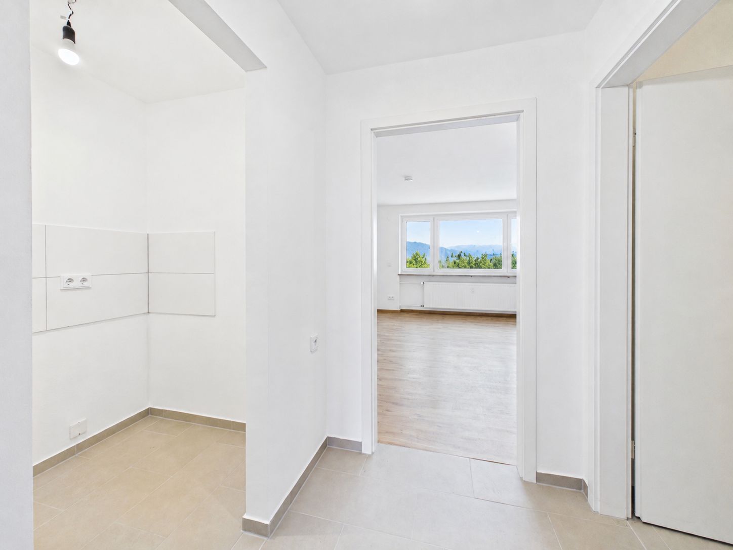 Heller Flur mit Blick in ein großes Wohnzimmer mit Parkett und großen Fenstern.