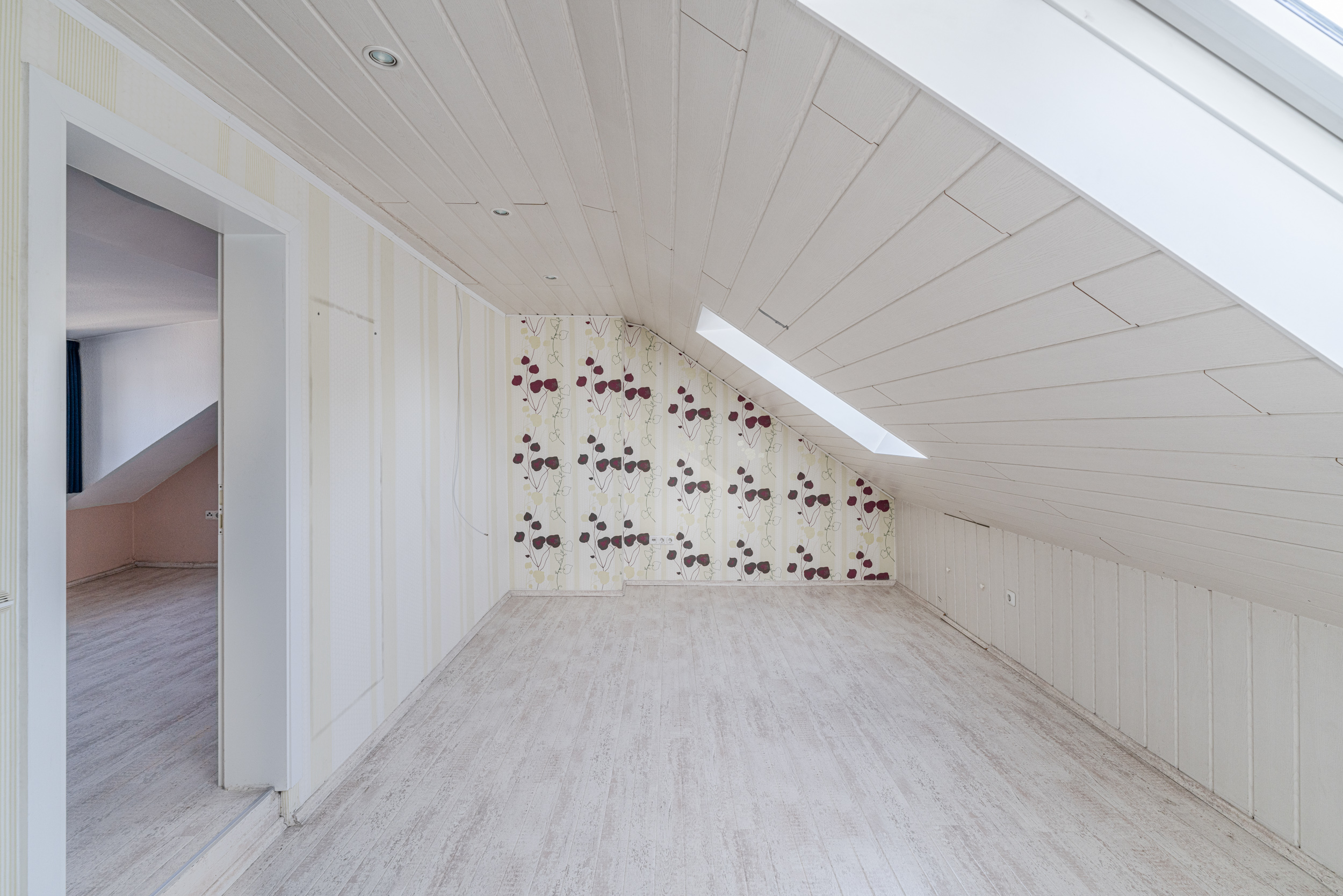 Leeres Dachzimmer mit schräger Decke, Tapete mit Muster und Dachfenster.