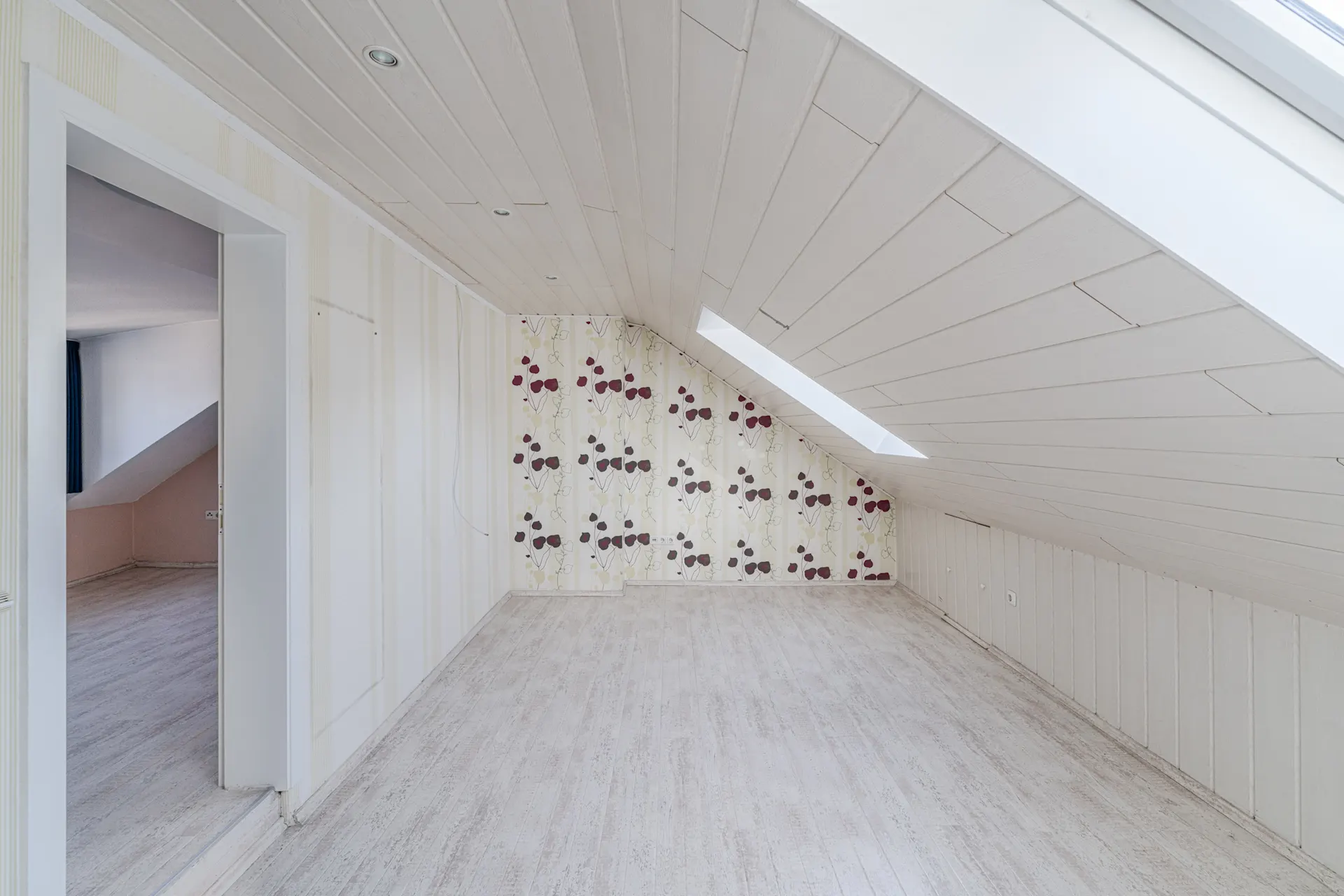 Leeres Dachzimmer mit schräger Decke, Tapete mit Muster und Dachfenster.