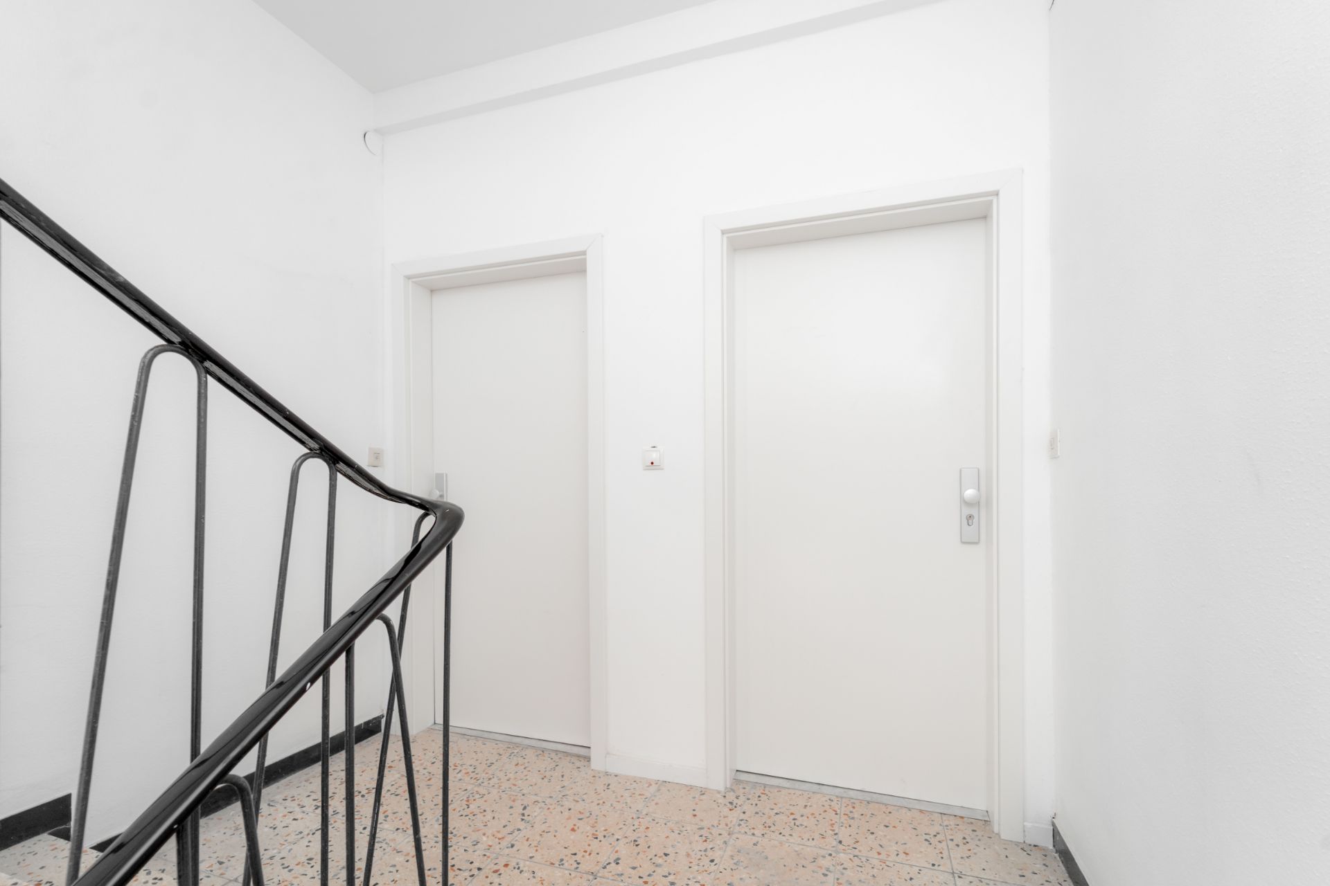 Flur mit zwei weißen Wohnungstüren und einem Treppengeländer.