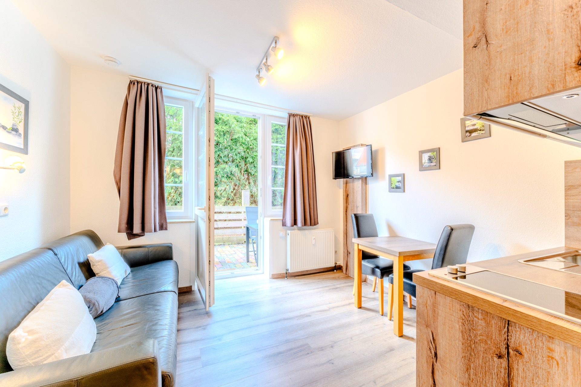 Helles Wohnzimmer mit Sofa, Esstisch, Fernseher und offenem Zugang zur Terrasse.