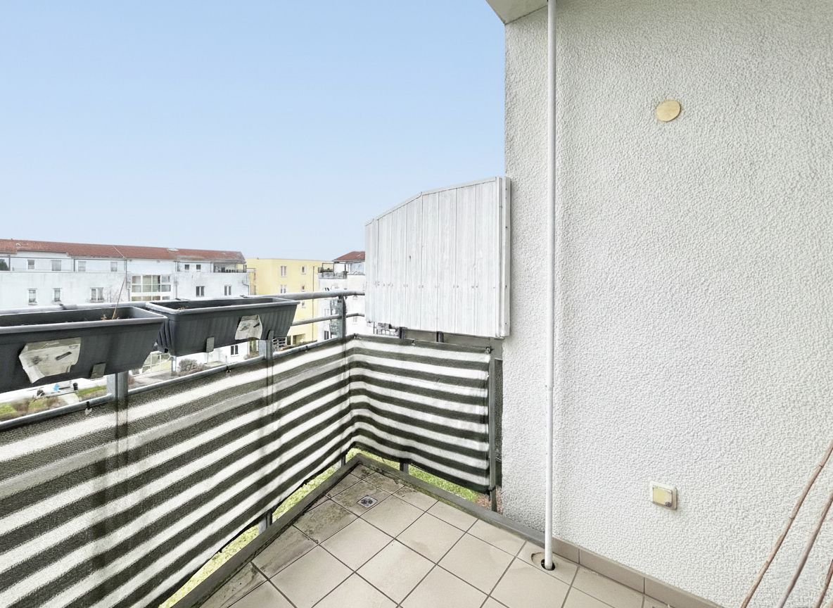 Kleiner Balkon mit gestreifter Sichtschutzmatte und zwei Pflanzenkästen an einem Wohnhaus.