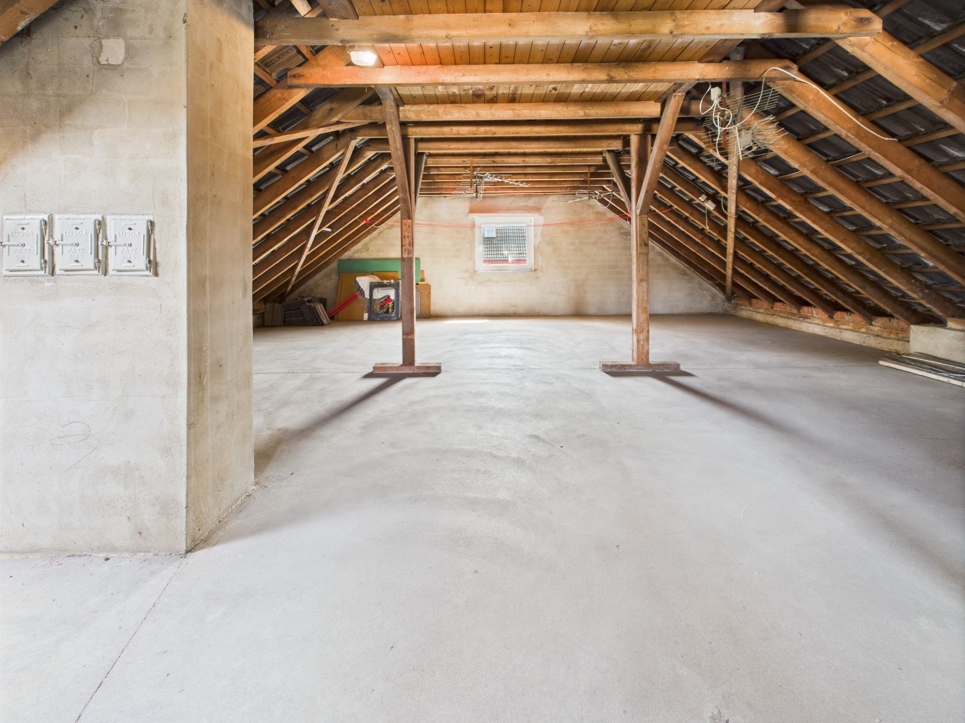 Geräumiger, leerer Dachboden mit sichtbaren Holzbalken und Fenster an der Stirnwand.