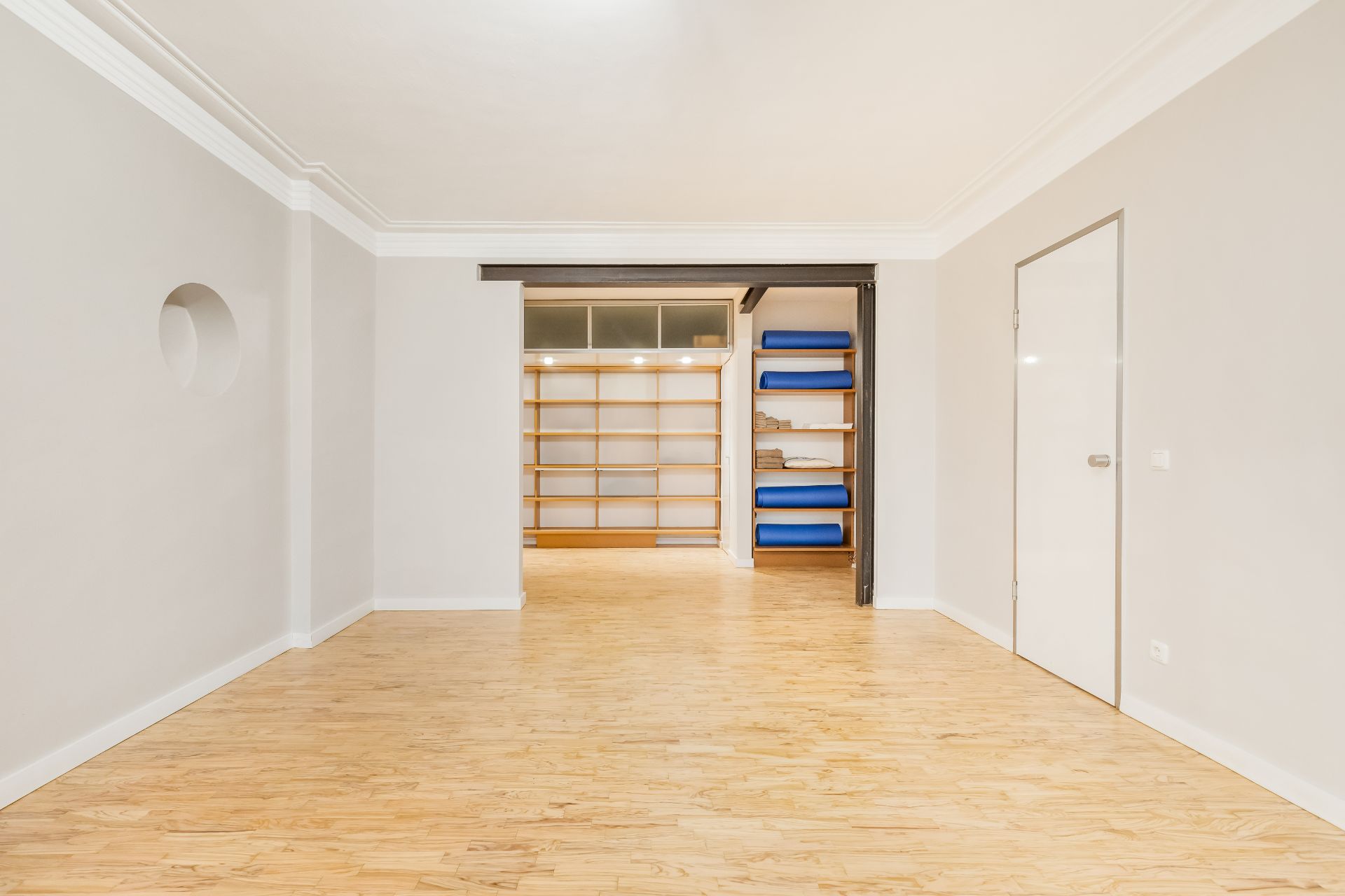 Heller Raum mit Holzfußboden, Regalwand und blauen Matten im Hintergrund.