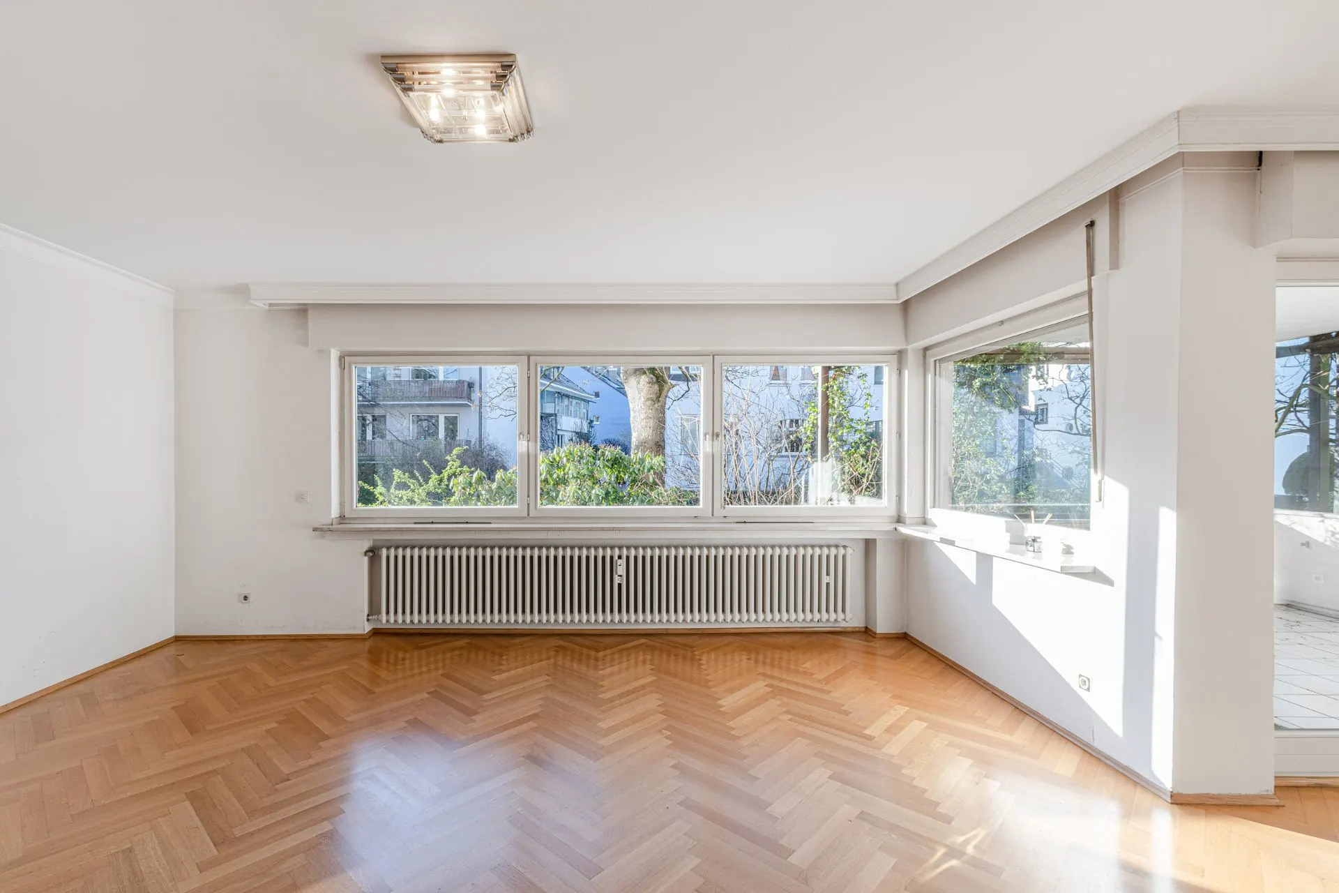 Helles Wohnzimmer mit Parkettboden, großen Fenstern und Blick ins Grüne.