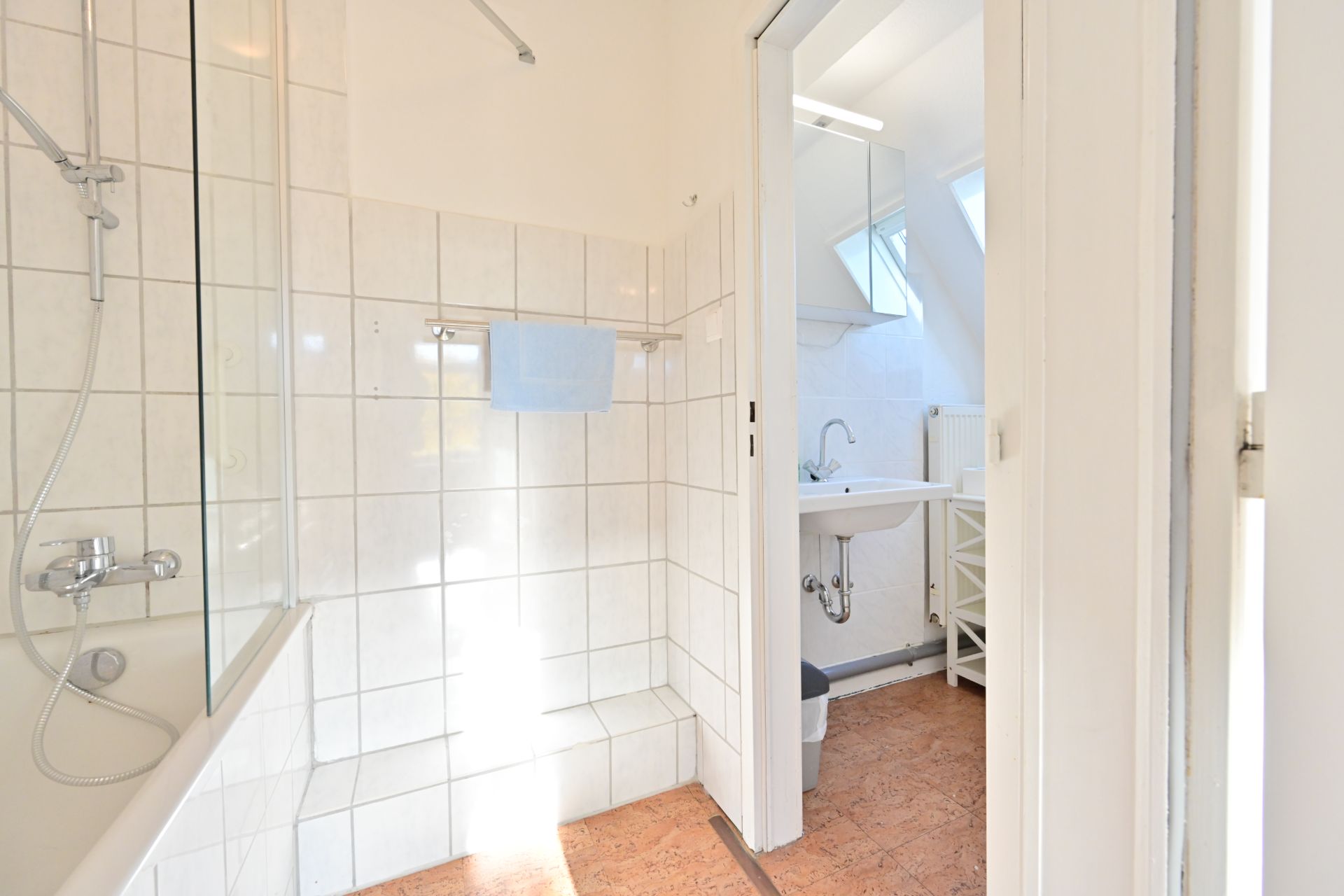 Helles Badezimmer mit Badewanne, Dusche, Waschbecken und Wandspiegel.