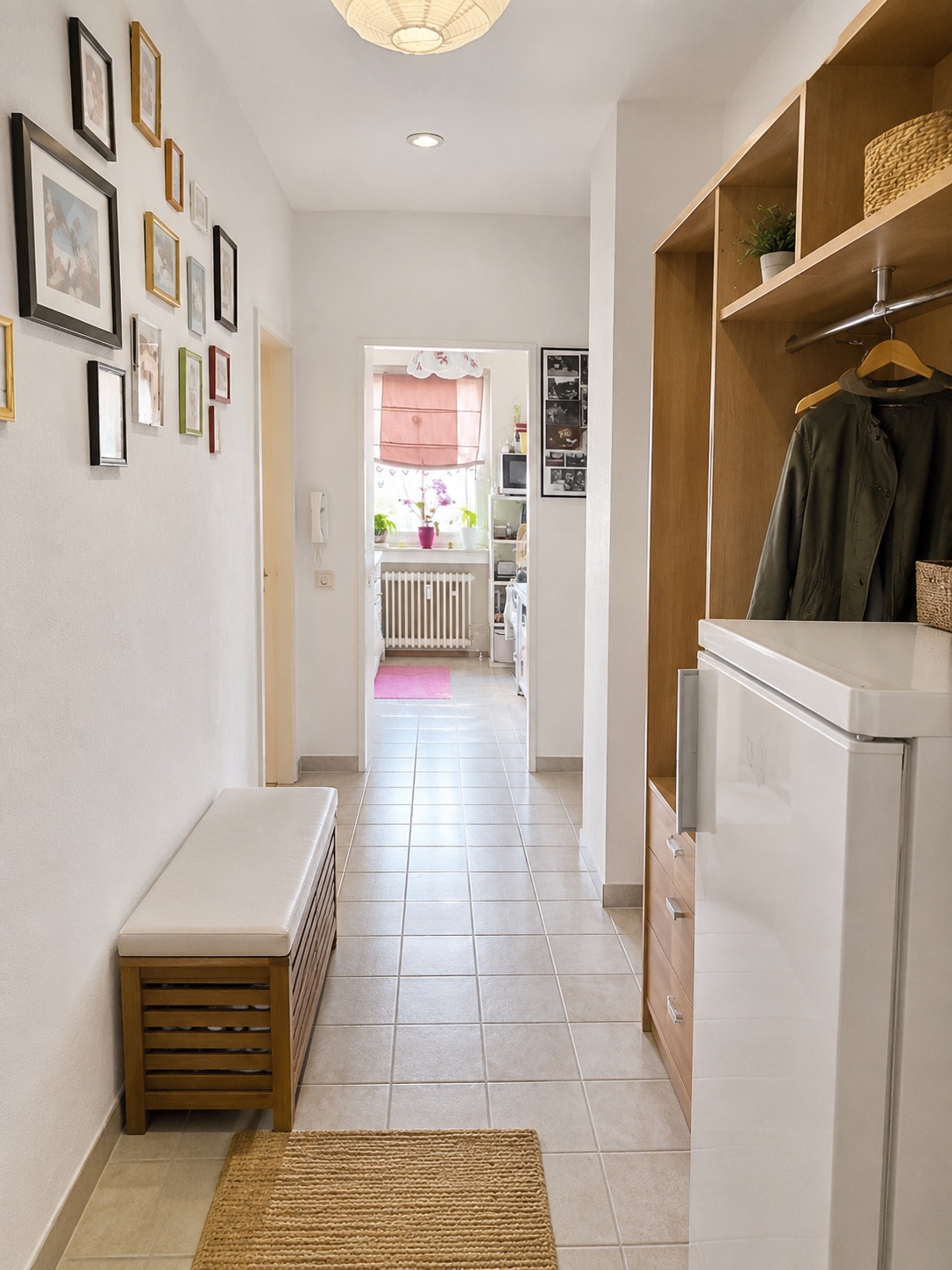 Heller Flur mit Bank, Garderobe, Kühlschrank und mehreren Bildern an der Wand.
