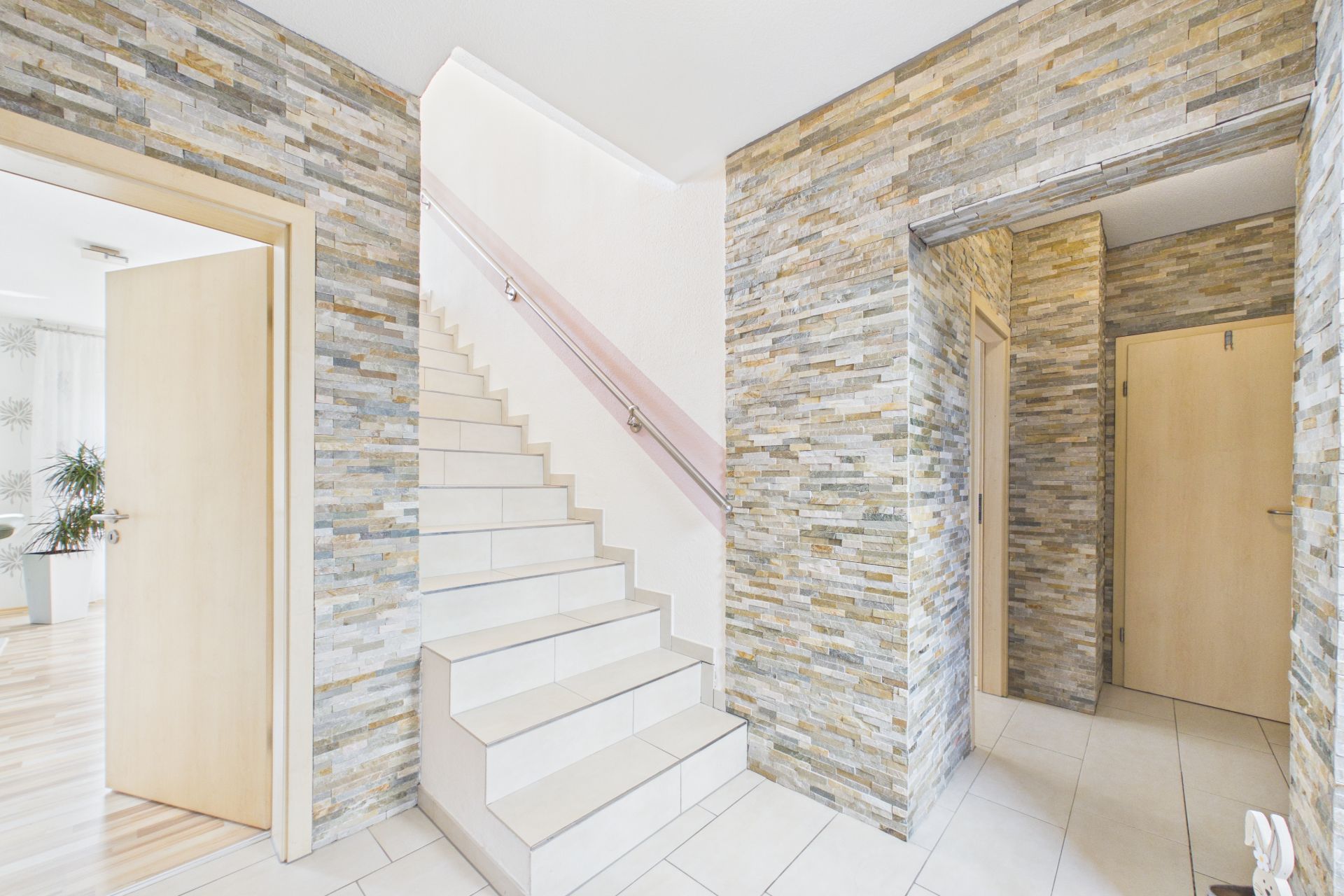Heller Flur mit Treppe, Steinwänden und mehreren offenen Holztüren.