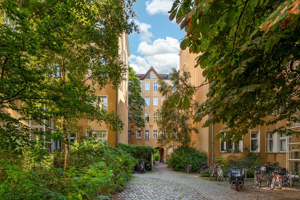 Begrünter Innenhof mit gelben Wohngebäuden, Fahrrädern und Kopfsteinpflasterweg.