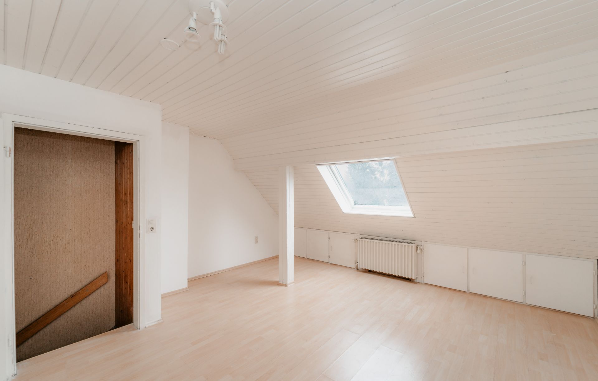 Heller Dachbodenraum mit schrägem Fenster, weißer Holzdecke und hellem Laminatboden.