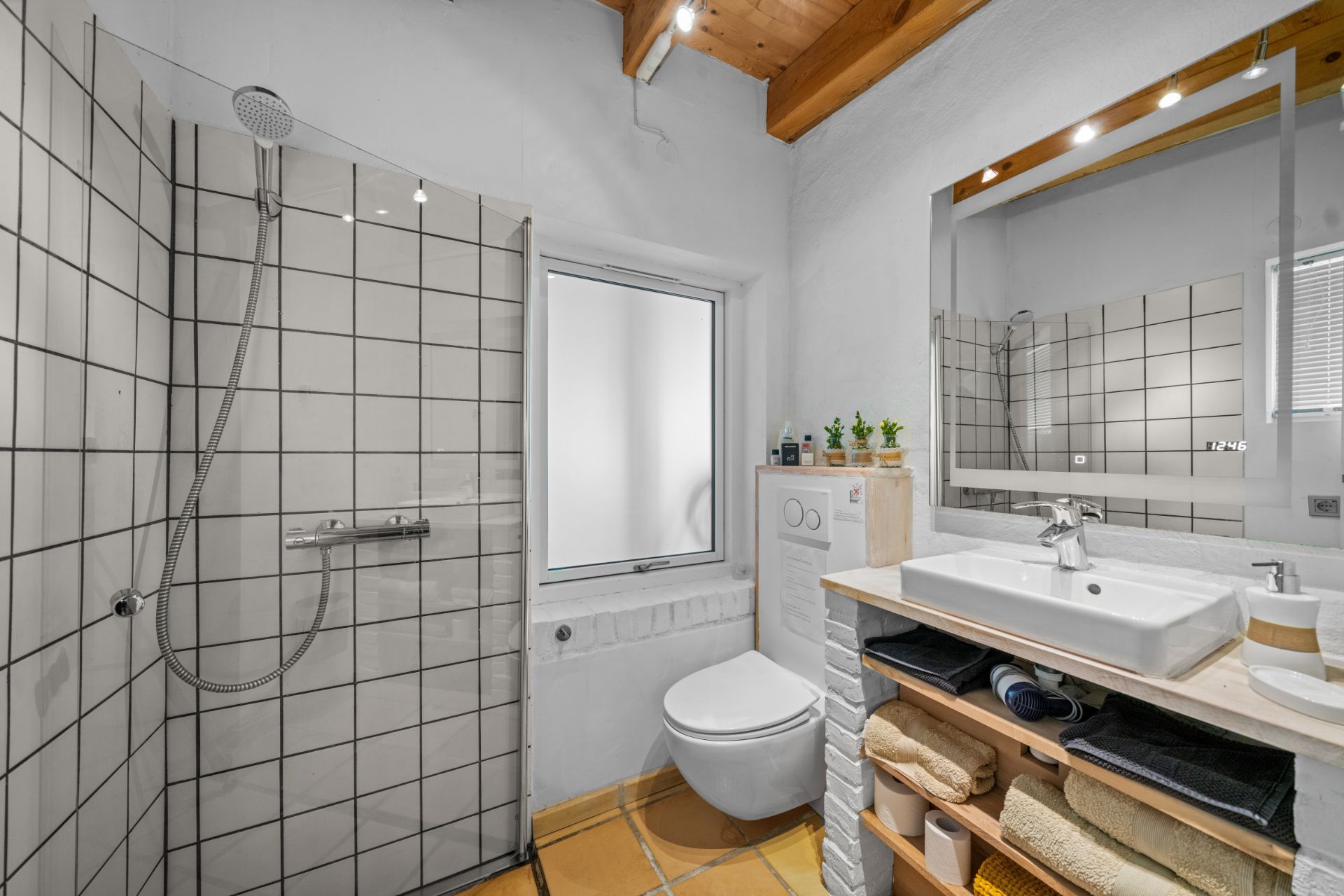 Modernes Badezimmer mit Dusche, WC, Waschbecken und Regal mit Handtüchern.