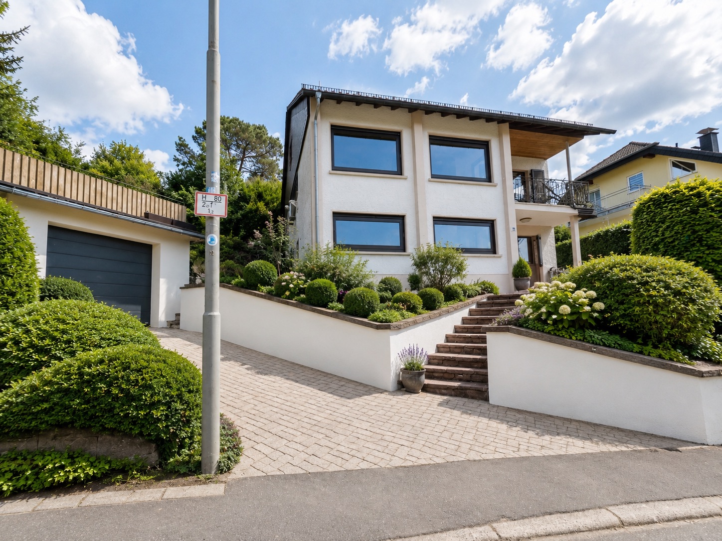 Modernes weißes Wohnhaus mit großem Garten, Treppe und Garage an einer Straße.