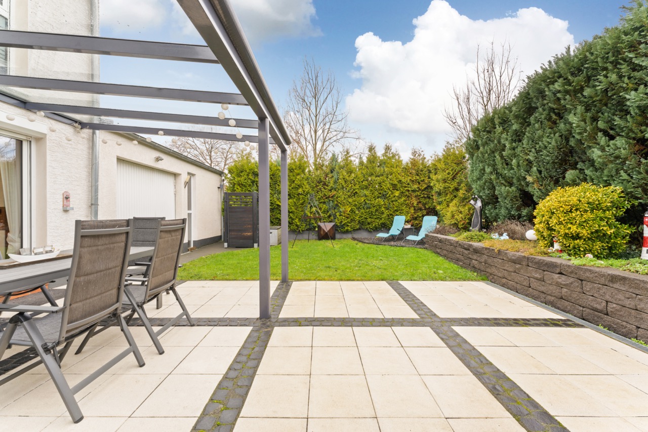 Moderne Terrasse mit Pergola, Esstisch, Gartenstühlen und angrenzendem Rasen im Hinterhof.