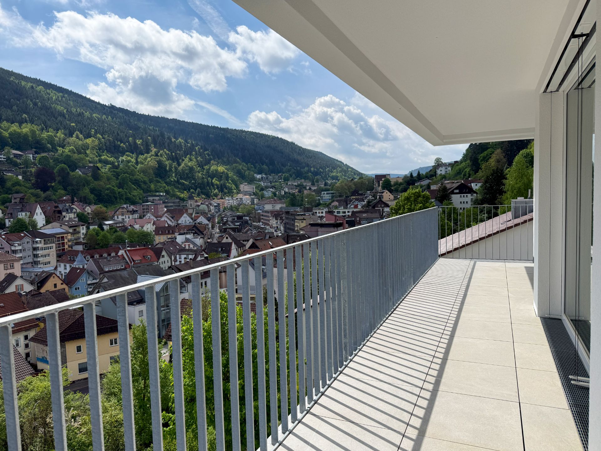 Großer Balkon mit Geländer und Blick auf eine Stadt und bewaldete Hügel.