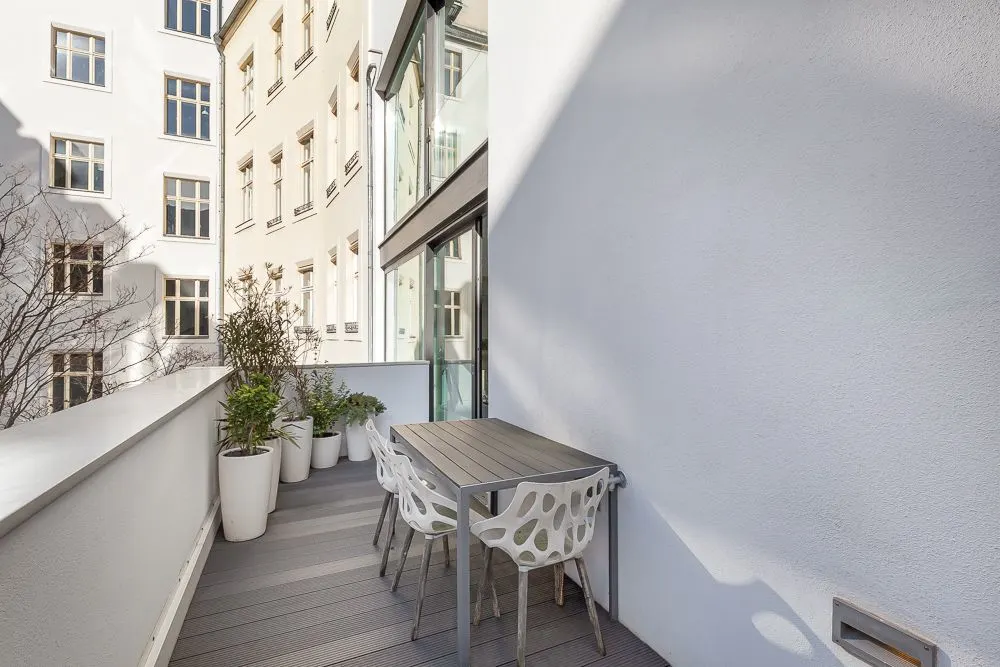 Moderner Balkon mit Tisch, vier Stühlen und mehreren Pflanzkübeln.